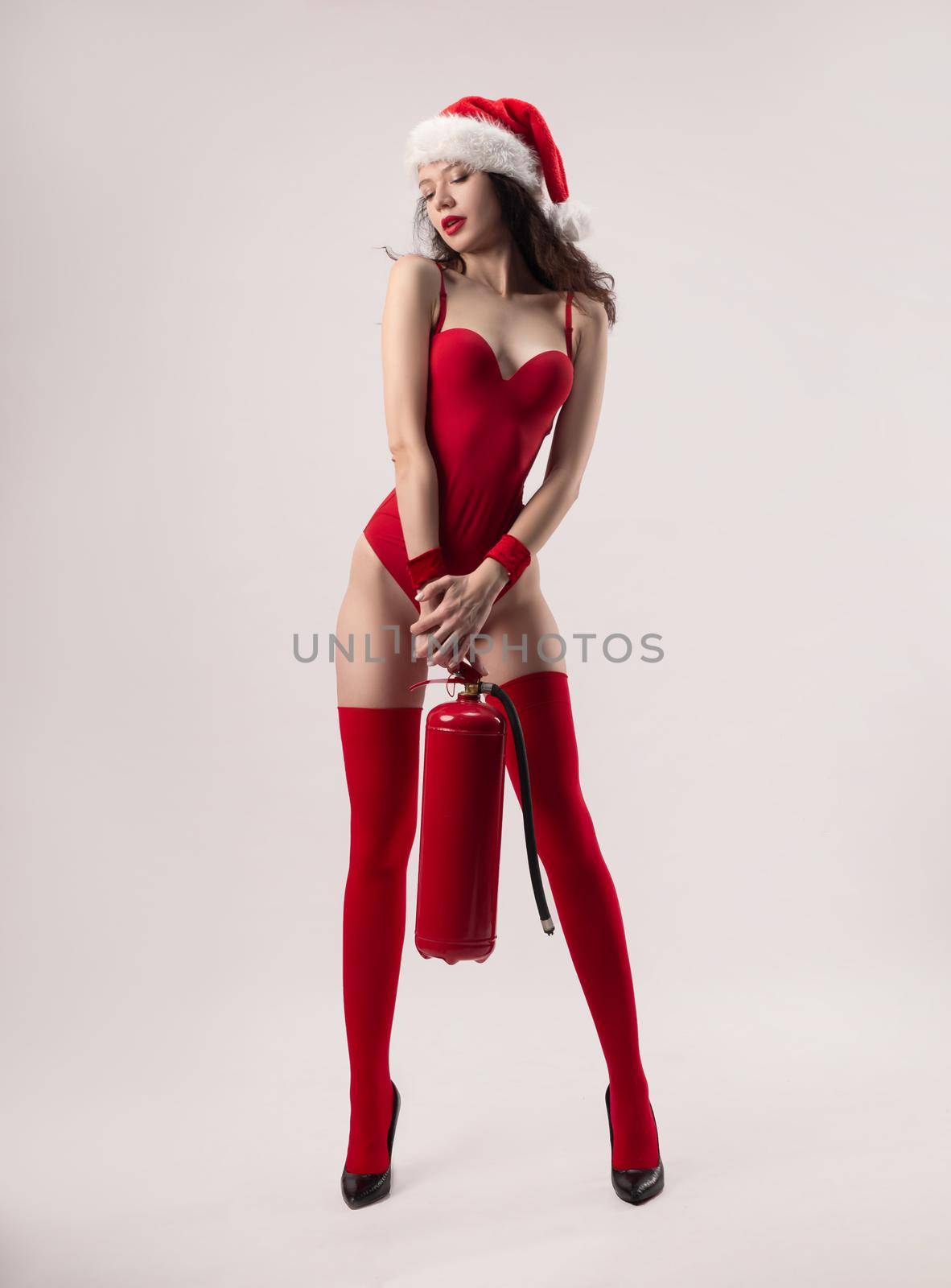 A woman in a Santa Claus Christmas hat in a red bodysuit poses sexually with a red fire extinguisher by Rotozey