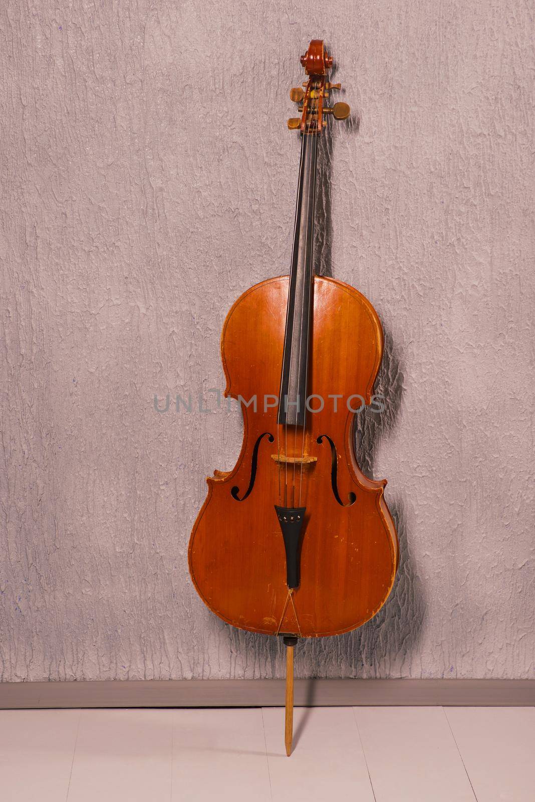 old battered cello standing near a gray textured wall by zartarn