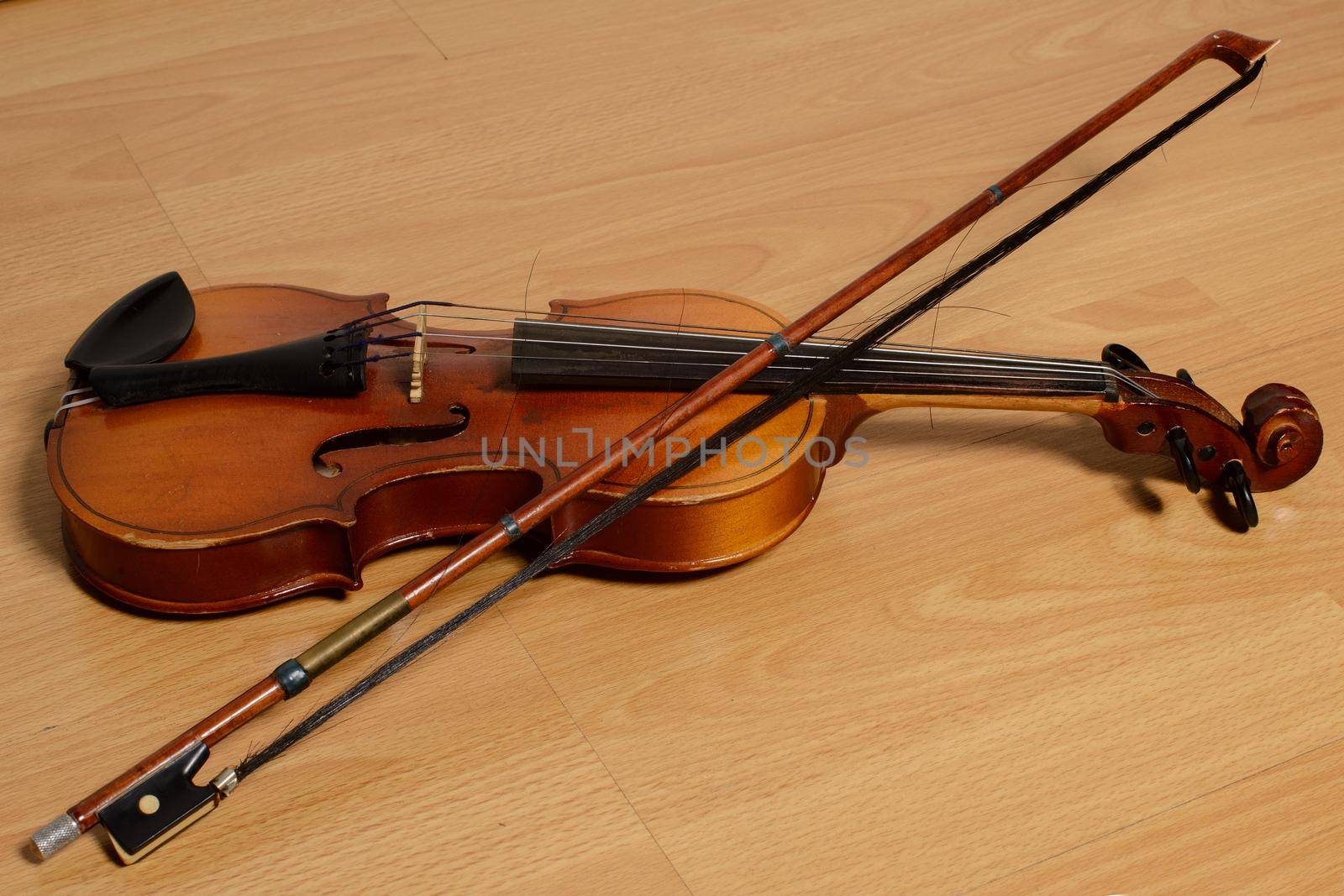 Old violin with a bow lies on a wooden bench