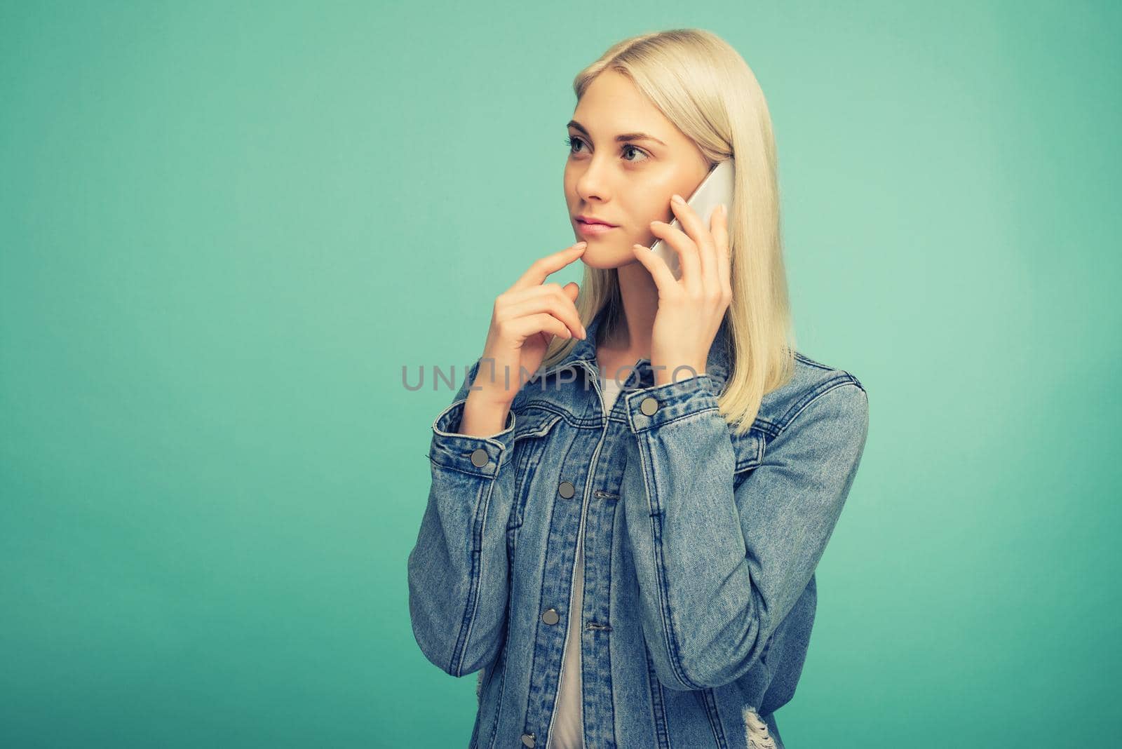 Pensive blonde girl speaks on smartphone isolated on blue background- image toned