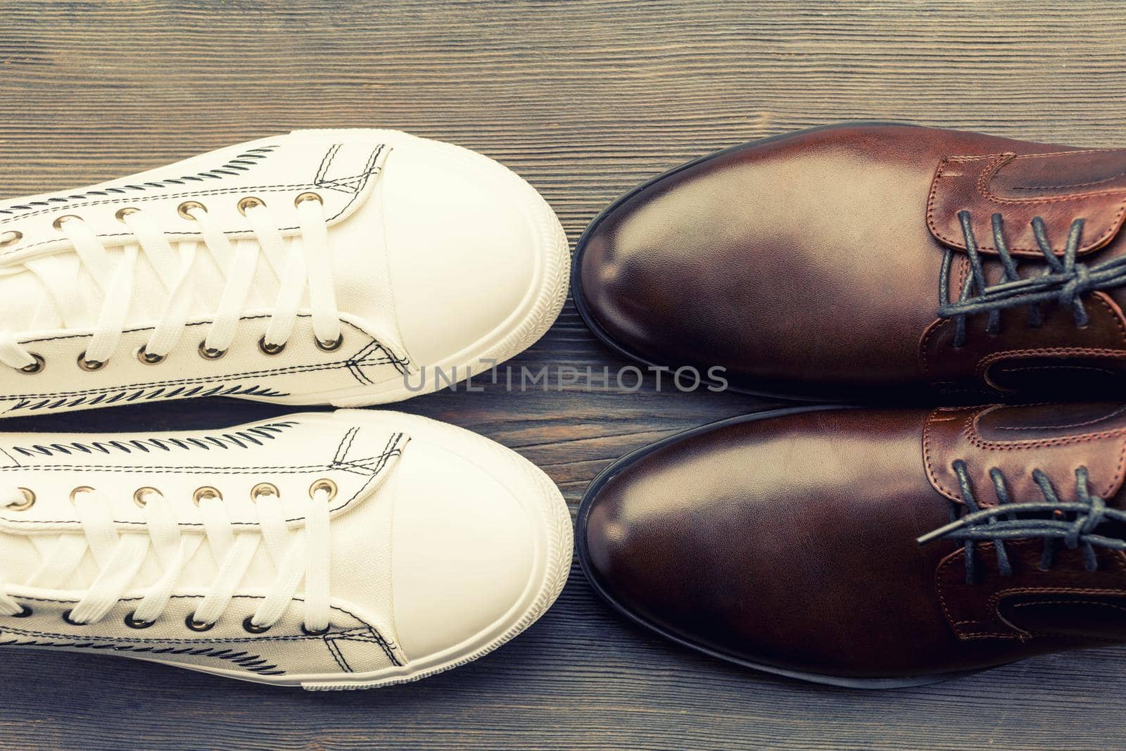 Men's classic brown shoes and white sneakers on a wooden background. Top view - image