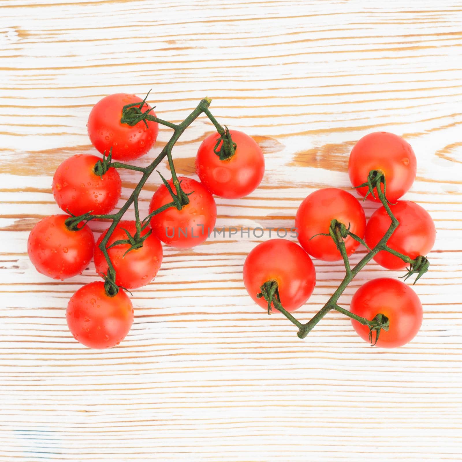 Ripe cherry tomatoes on a twig on a white woden background close up - image