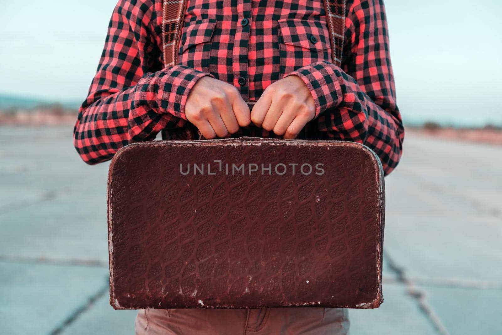 Woman holds small retro suitcase on road, face is not visible, space for text, theme of travel