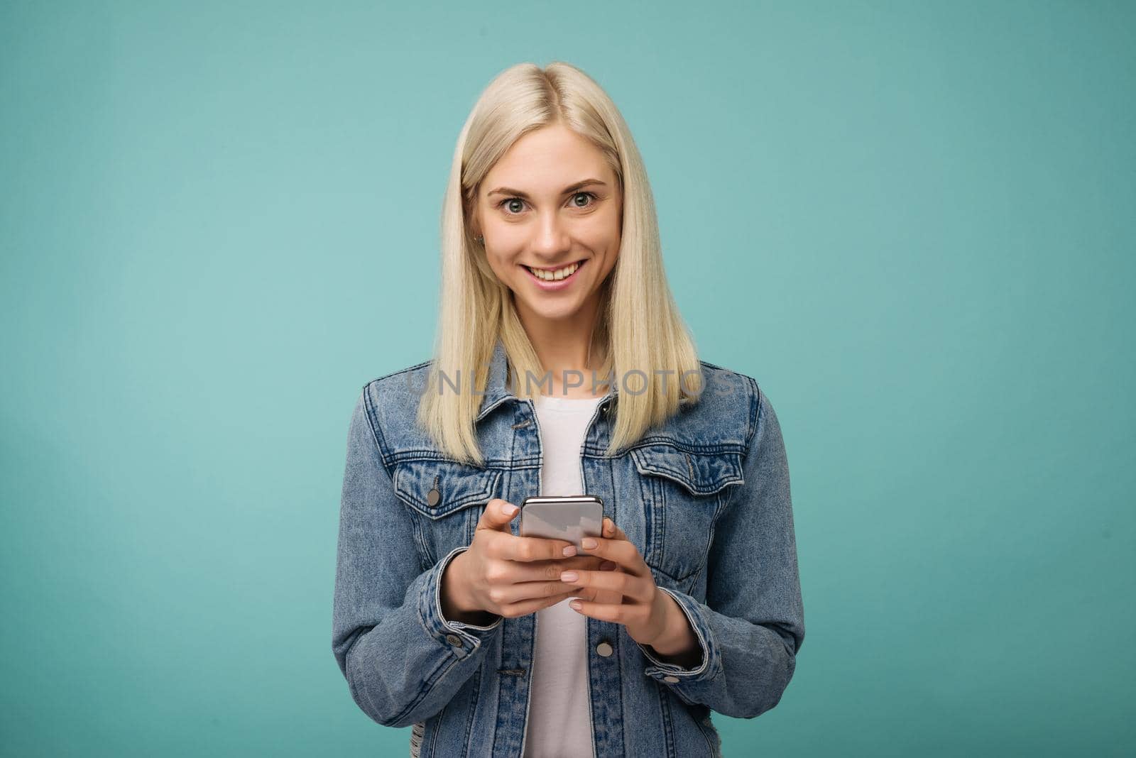 Young beautiful happy woman using smart phone. Isolated on blue background