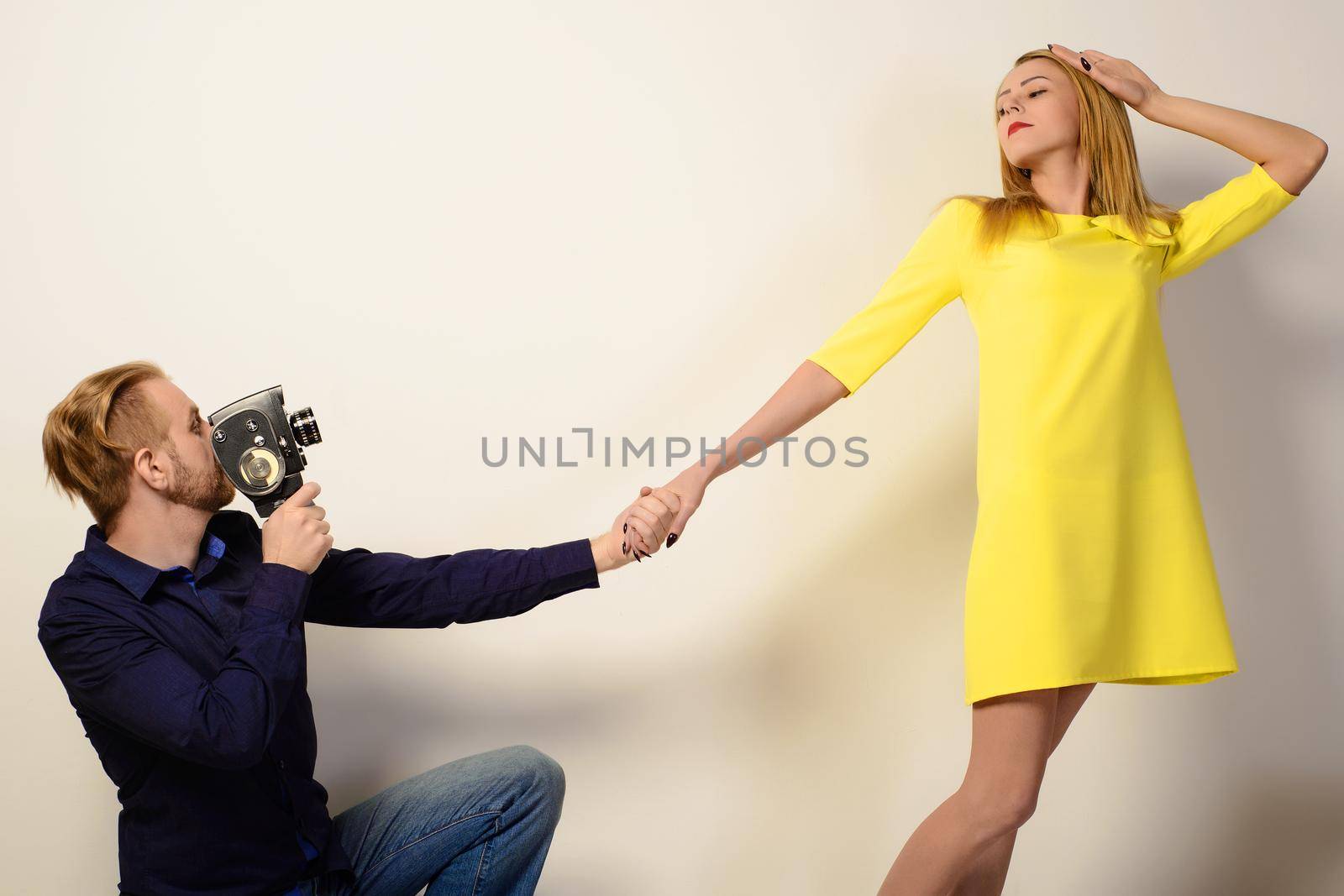 Stylish man in a blue shirt is filming a slim woman in a yellow dress with an old camera
