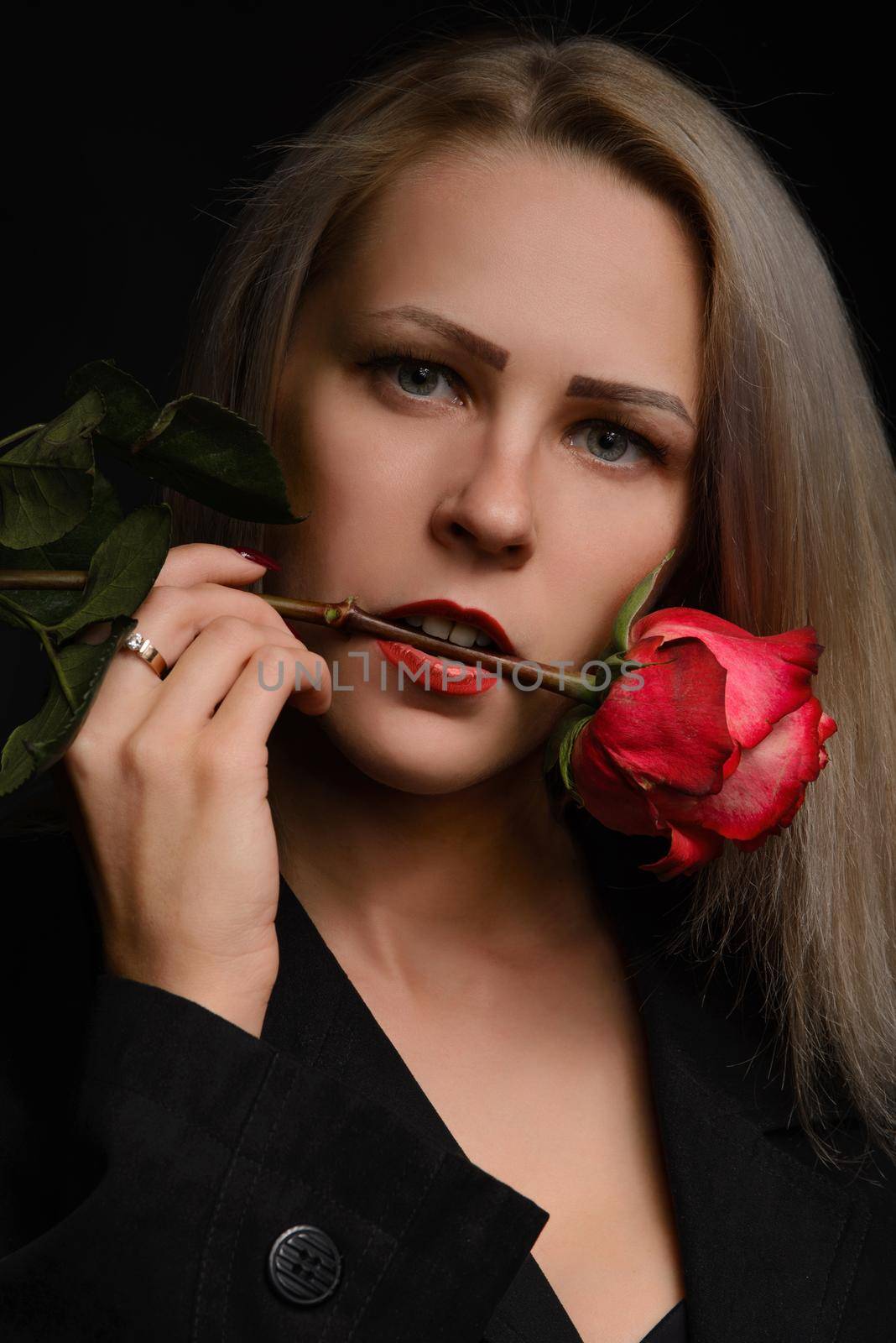 Studio shot. Passionate professional model posing with red rose in her mouth isolated on dark backround.