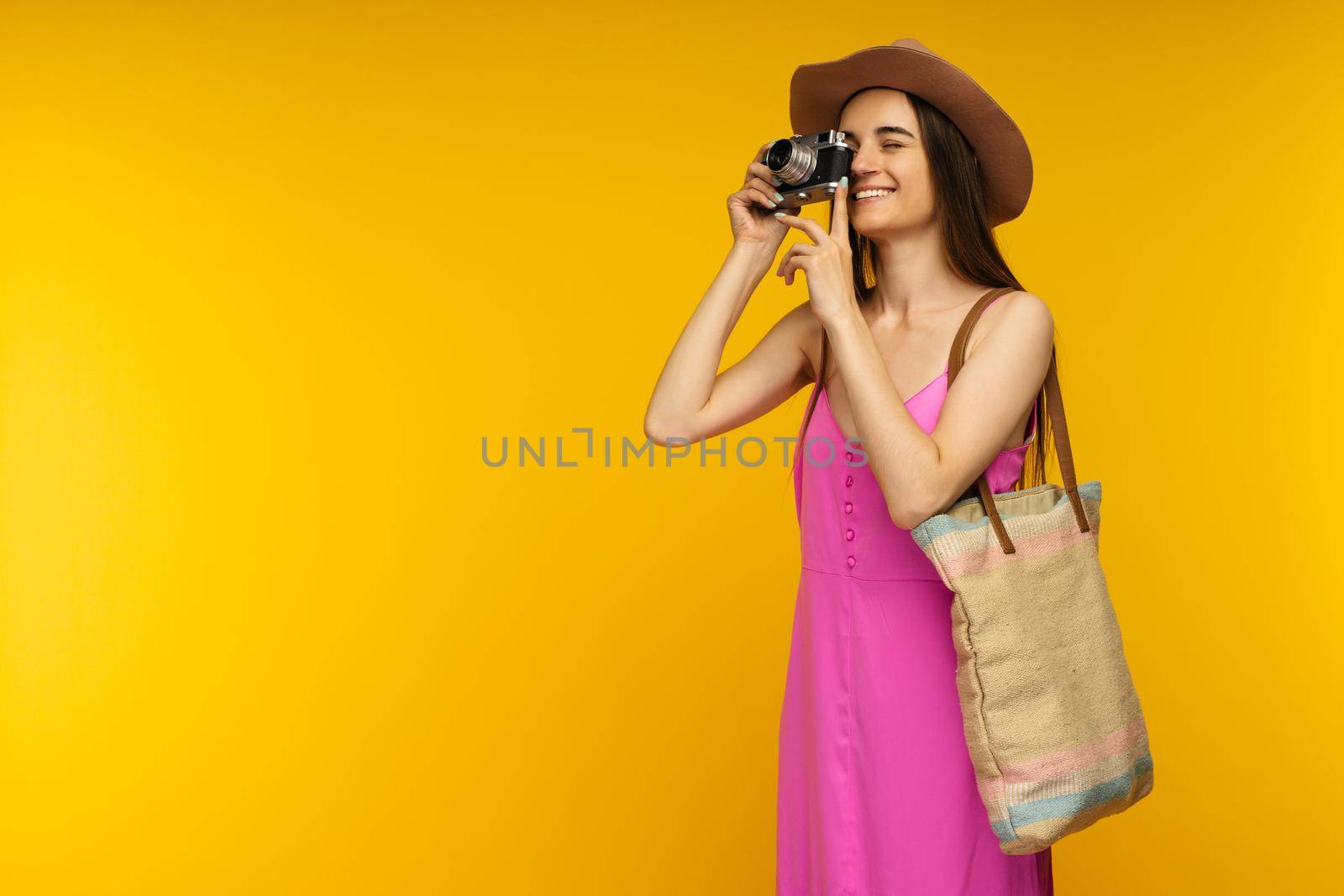 Happy girl in a pink dress and sunglasses holding camera on a yellow background- image