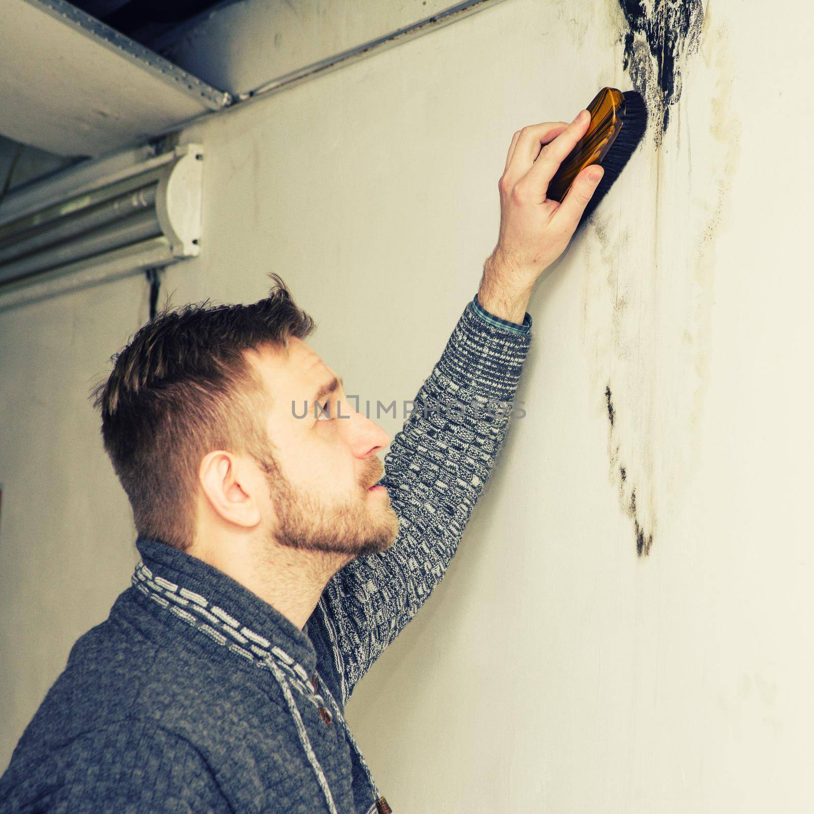 Bearded man removes black mold on the wall after leakage - Image Toned