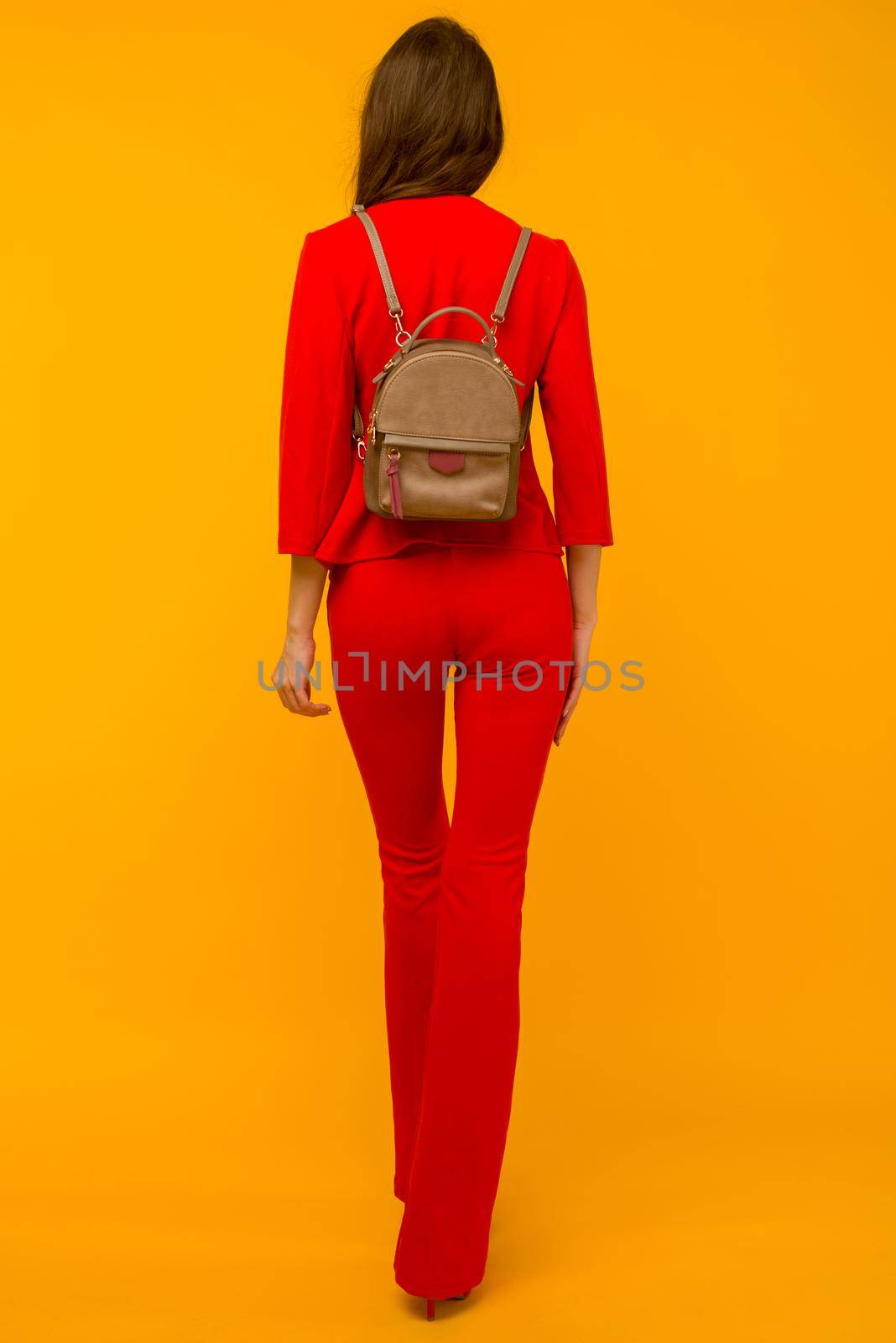 Young girl in a red suit with a small backpack on a yellow background - image