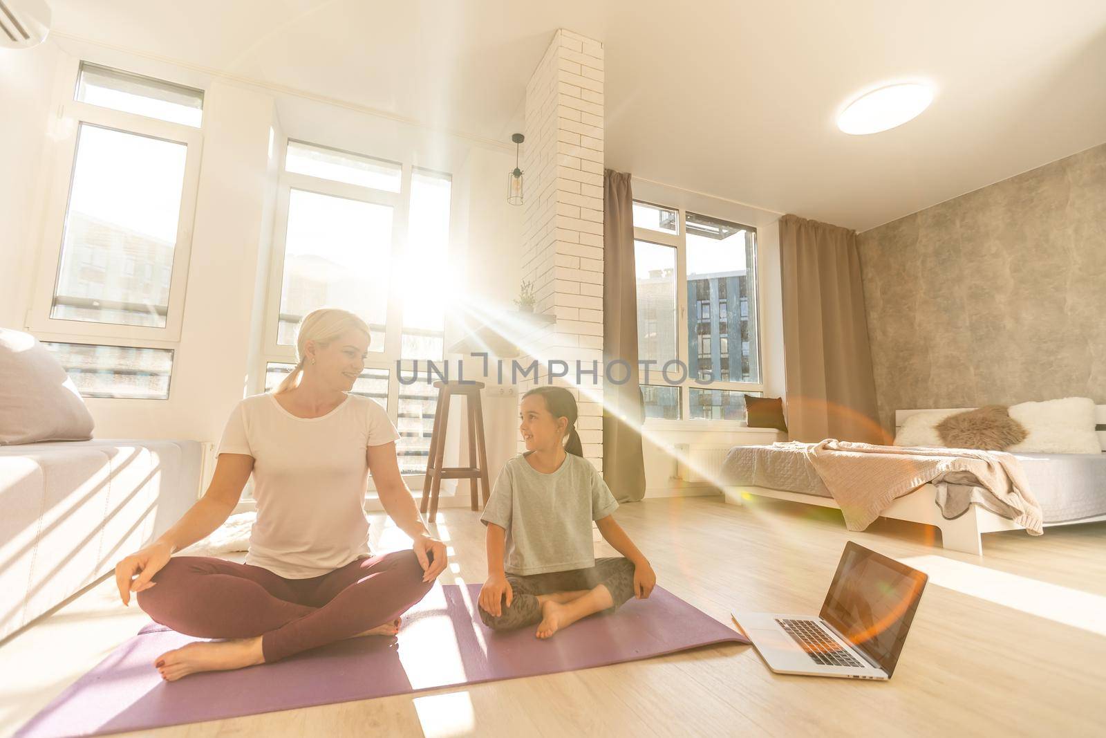 Young adult mother with her daughter watching online training together at home, looking a laptop