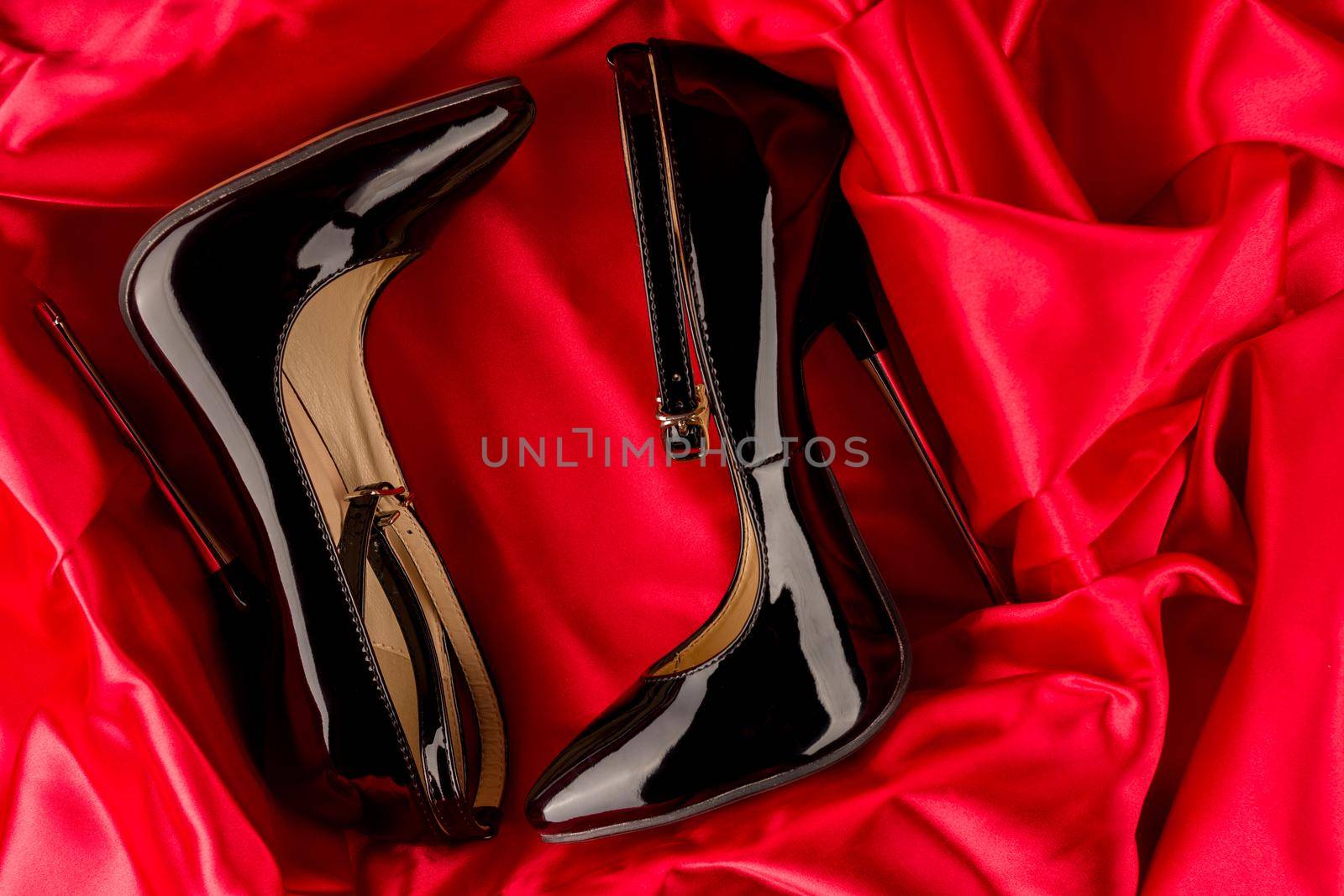 Black fetish shiny patent leather stiletto high heels with ankle strap on red satin background