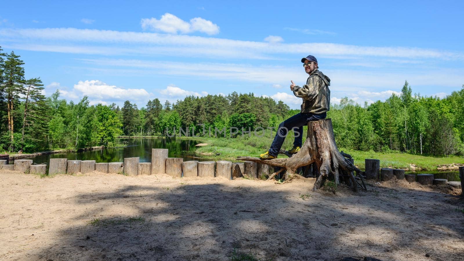 Smiling man tourist is sitting on a tree stump side of the river.Summer forest