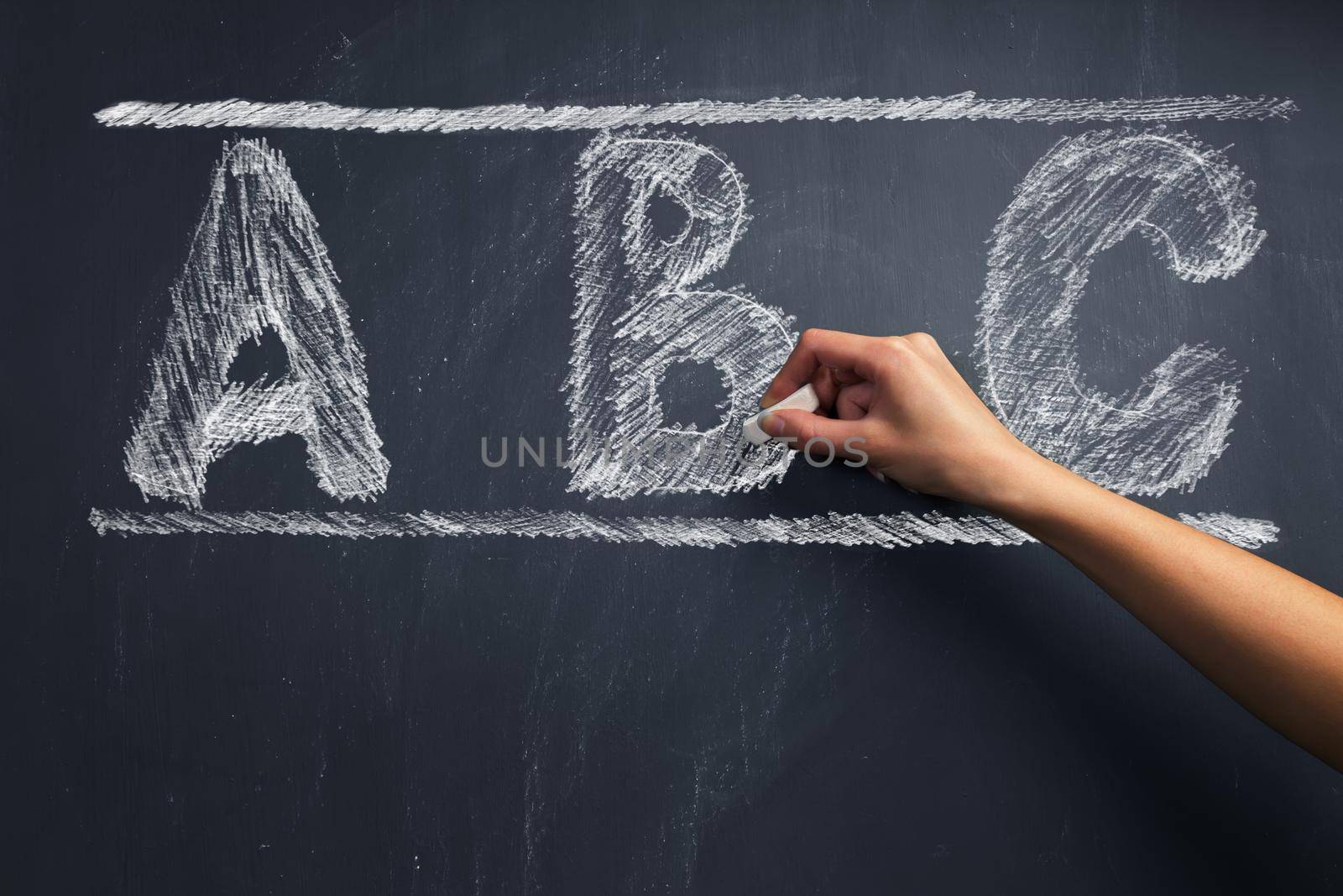 Human hand writes ABC alphabet on blackboard