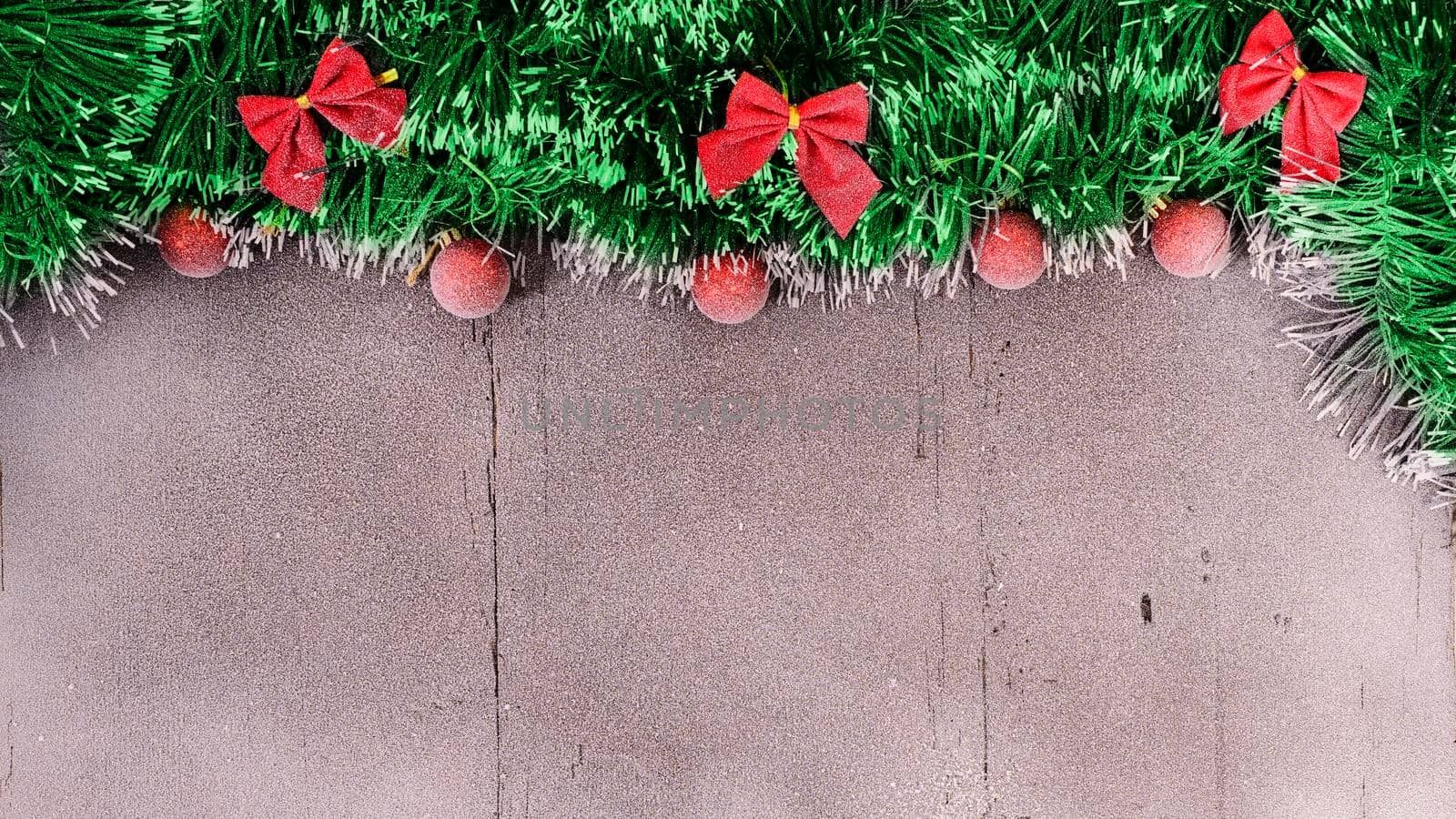 Christmas card. Red balls, tinsel and bow on a snow-covered wooden background with empty spase