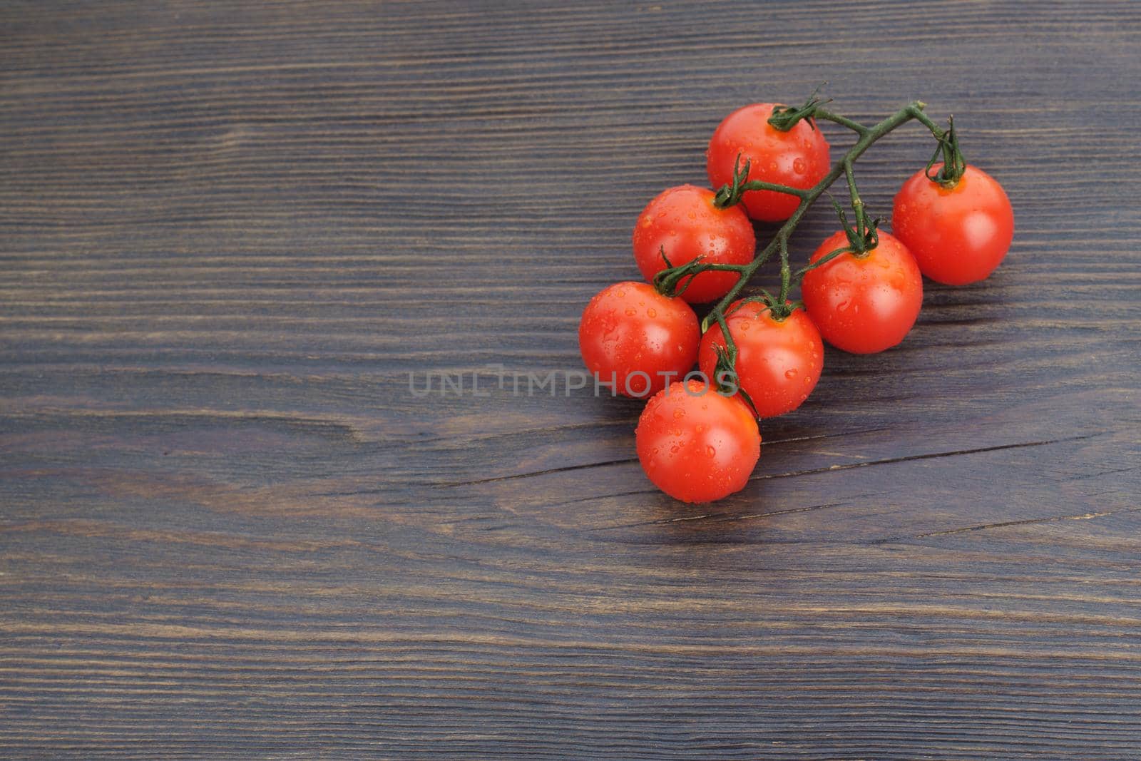 Ripe cherry tomatoes on a twig on a dark woden background - image
