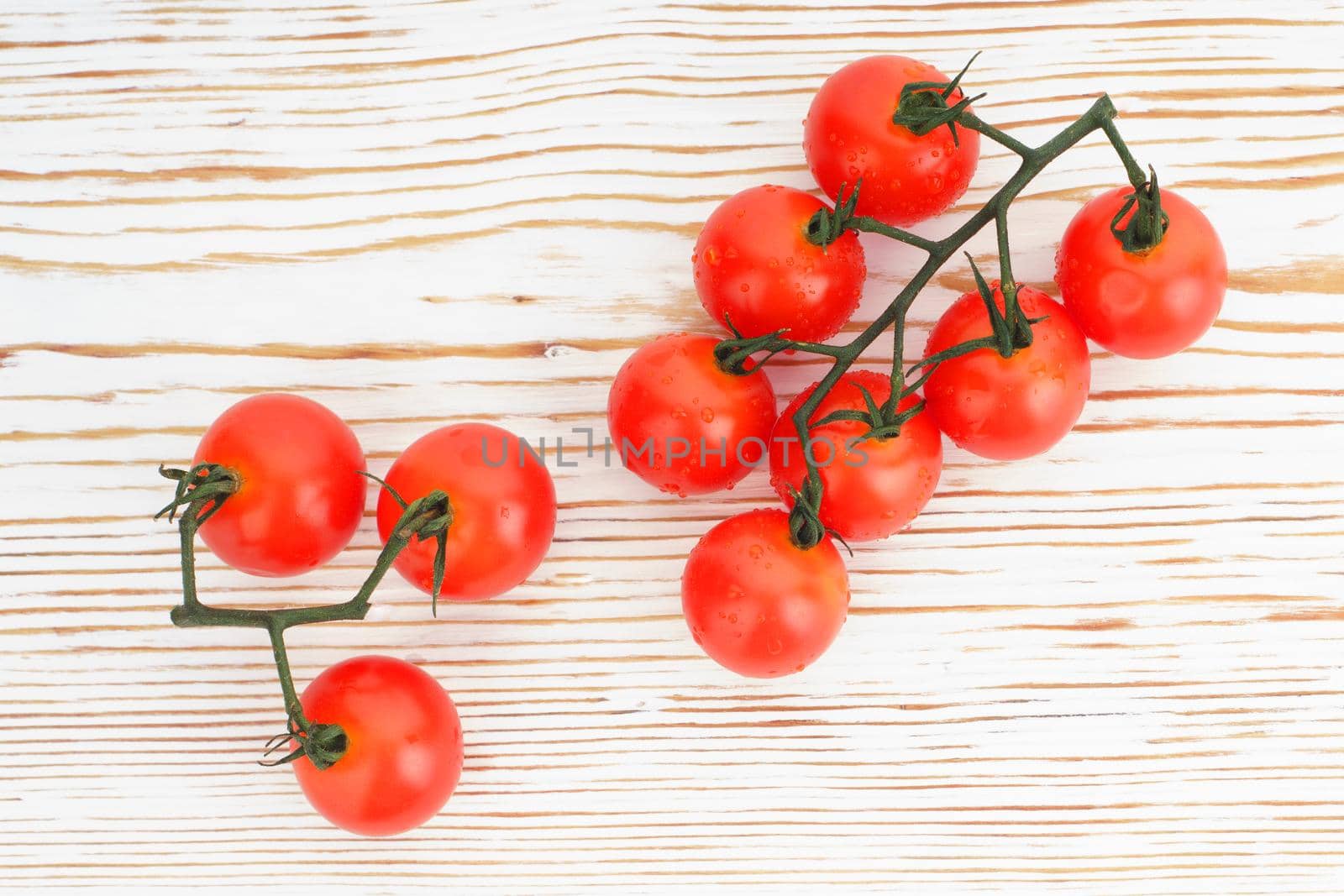 Ripe cherry tomatoes on a twig on a white woden background close up - image