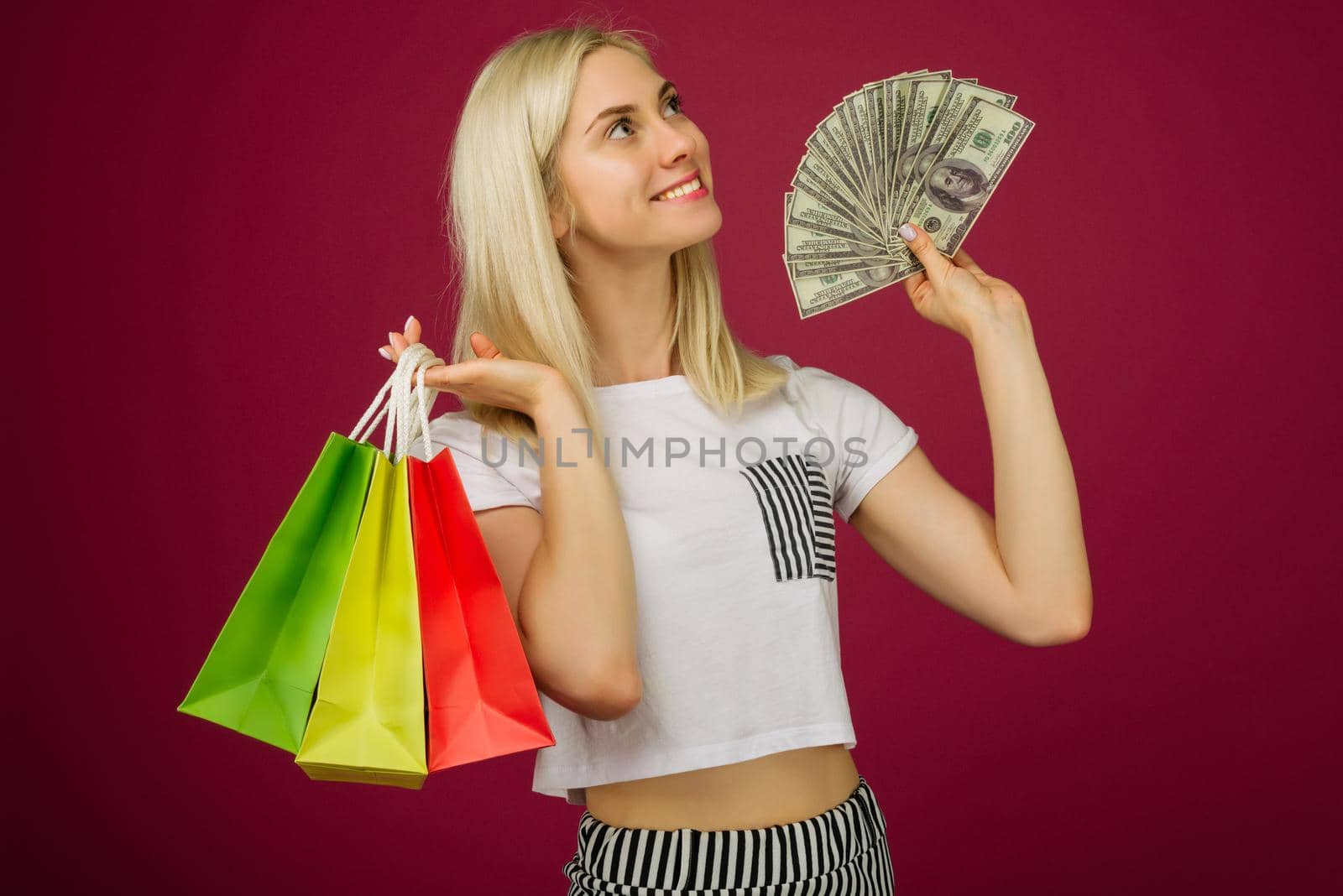Happy girl in holds one hundred dollars bills and shopping bags on ruby background