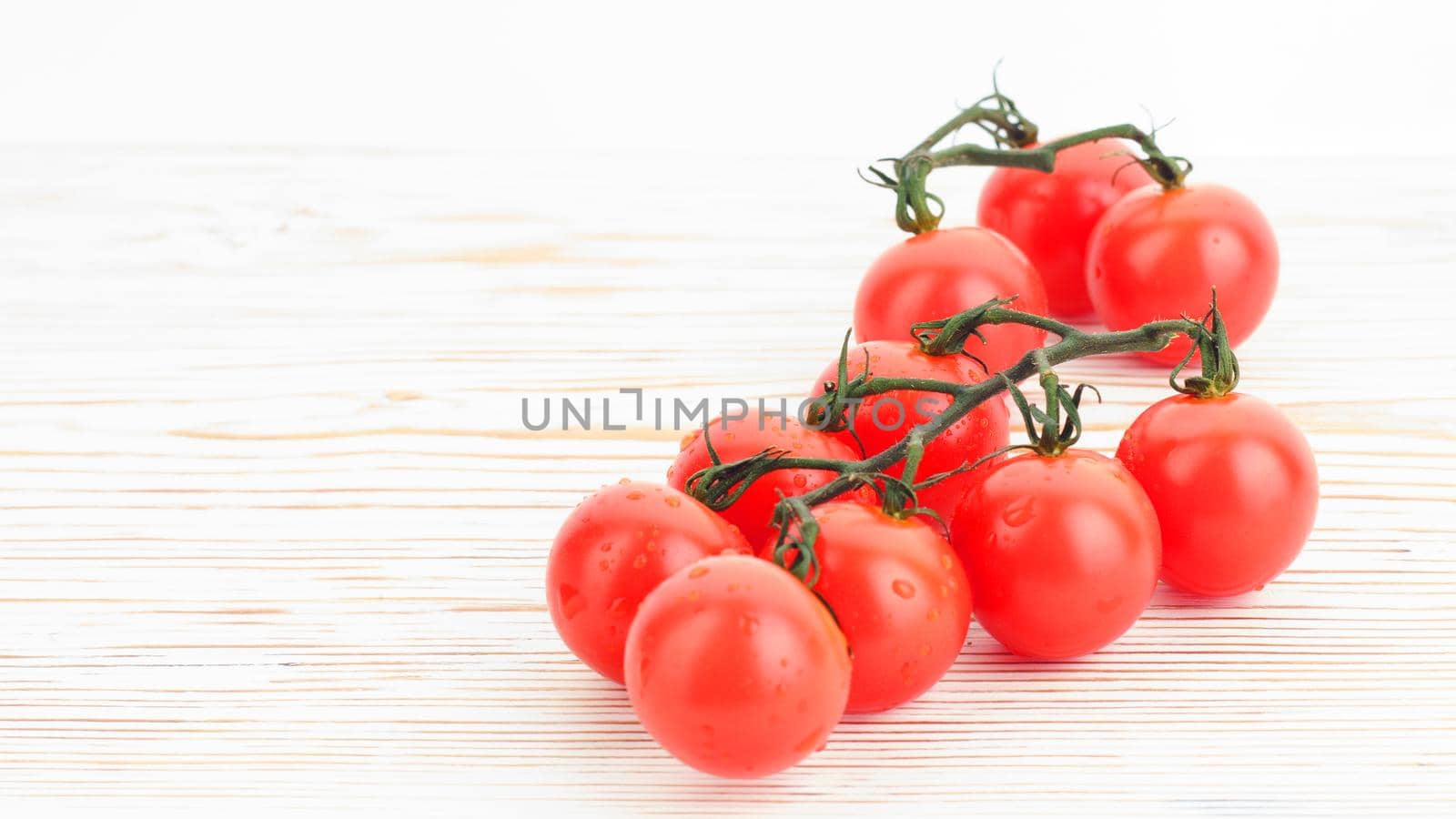 Ripe cherry tomatoes on a twig on a white woden background close up - image