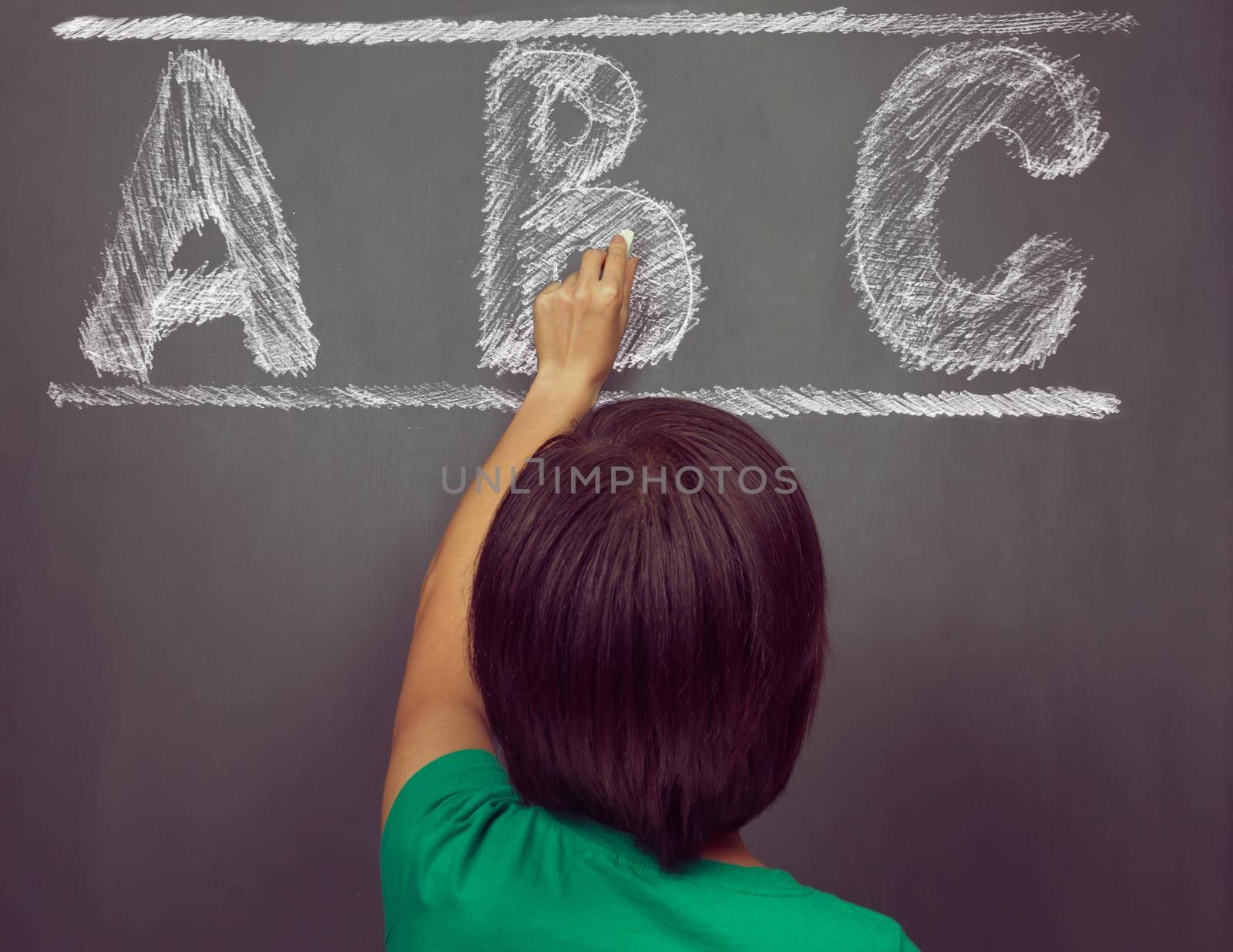 Unrecognizable woman writes ABC alphabet on blackboard, rear view