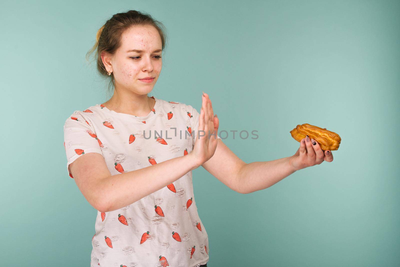 Portrait of pimply teen girl hows hands stop on a delicious cake on blue background