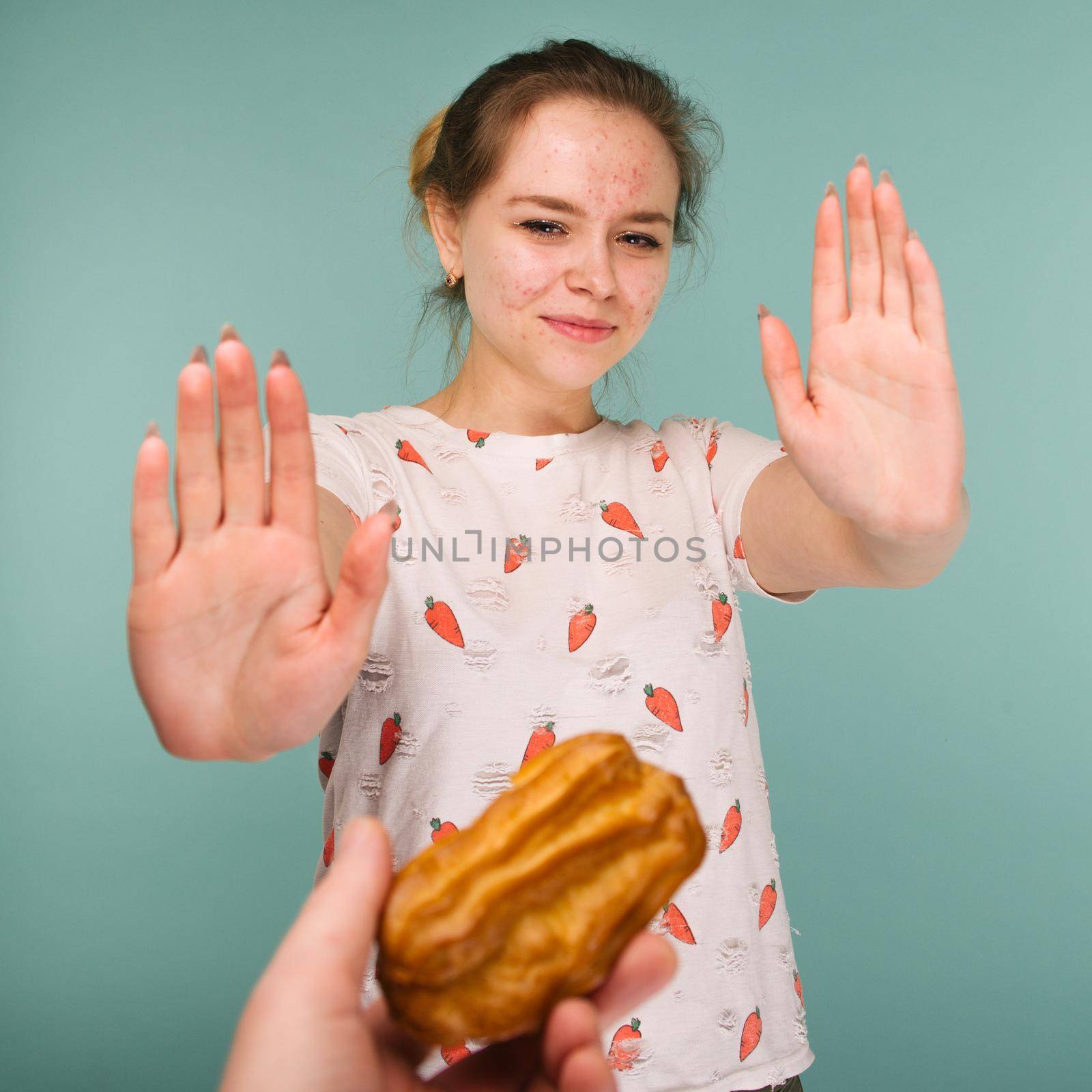 Portrait of pimply teen girl hows hands stop on a delicious cake on blue background