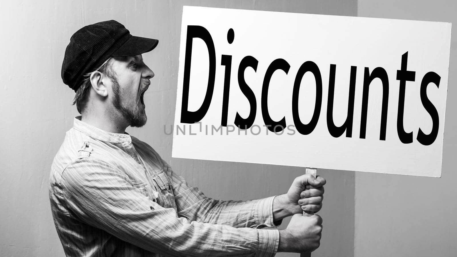 Bearded male worker in a cap shouts with a poster in his hands. Inscription discounts. Shopping concept.