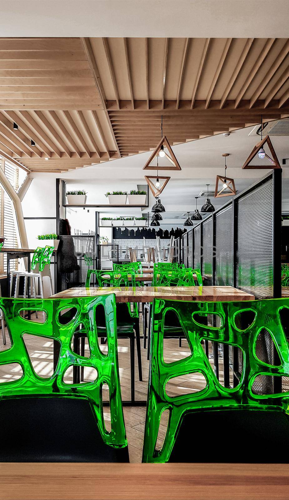 Cafeteria, no people dining room with wooden tables and green chairs. Interior with wood and metal elements. Modern dining areas with window lighting. Ukraine, Kiev - February 19, 2021.