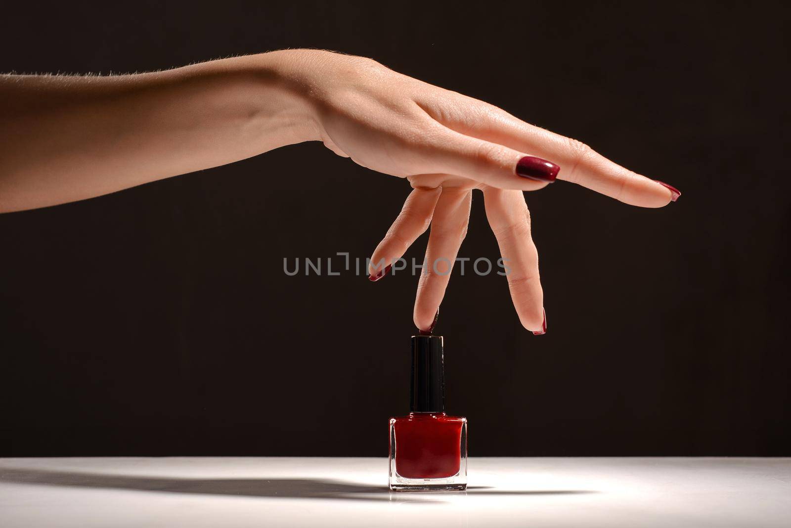 Beauty Hand with red manicure and nail polish bottle.