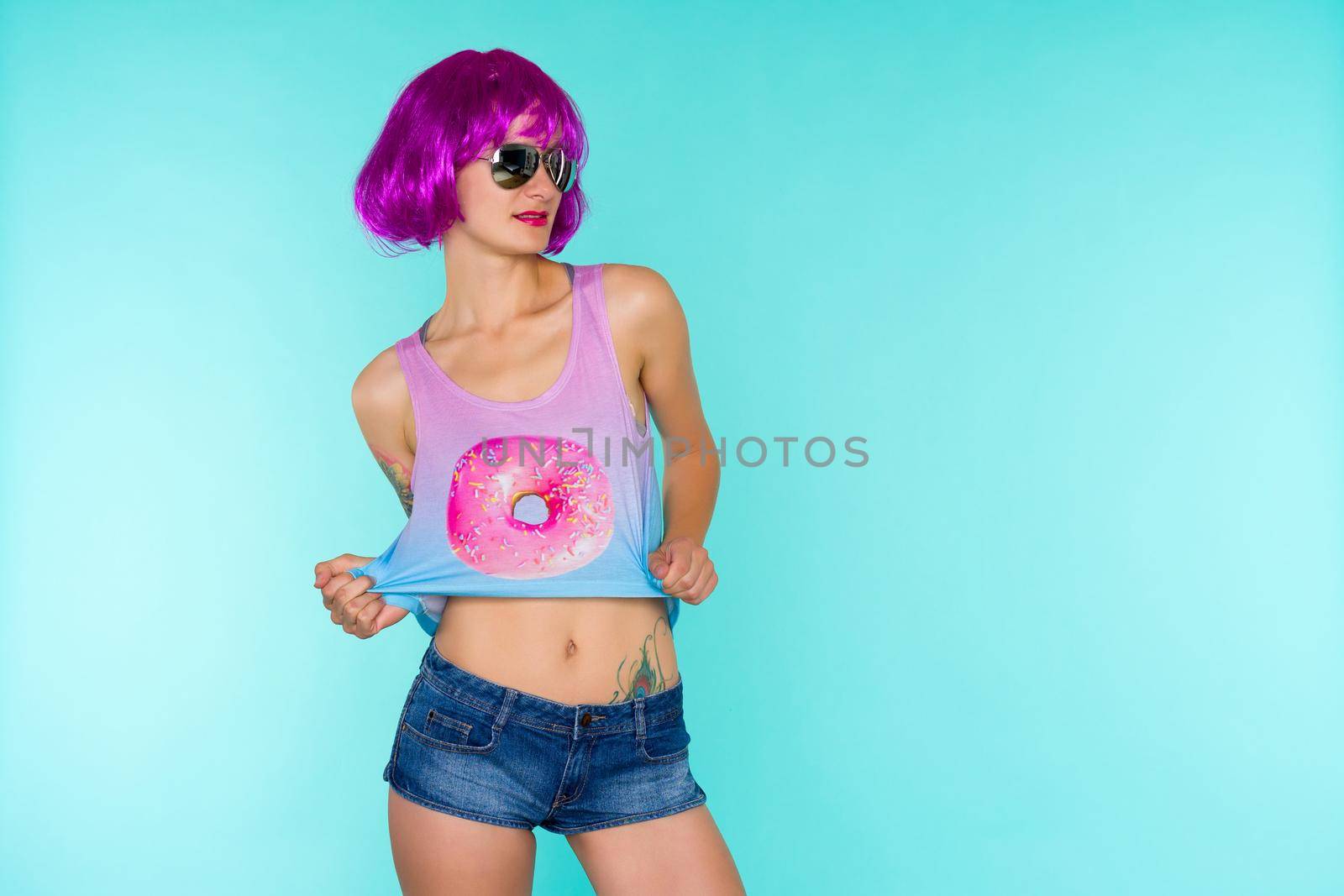 Portrait of young transgender woman in pink wig and sunglasses on blue background - image