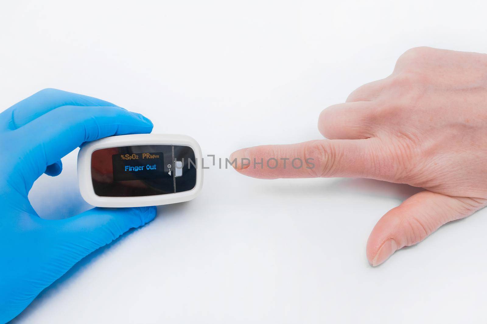 The doctor's hand in a latex medical glove holds a device to measure oxygen in the blood, pulsexymeter with the finger of an elderly woman on a white background.