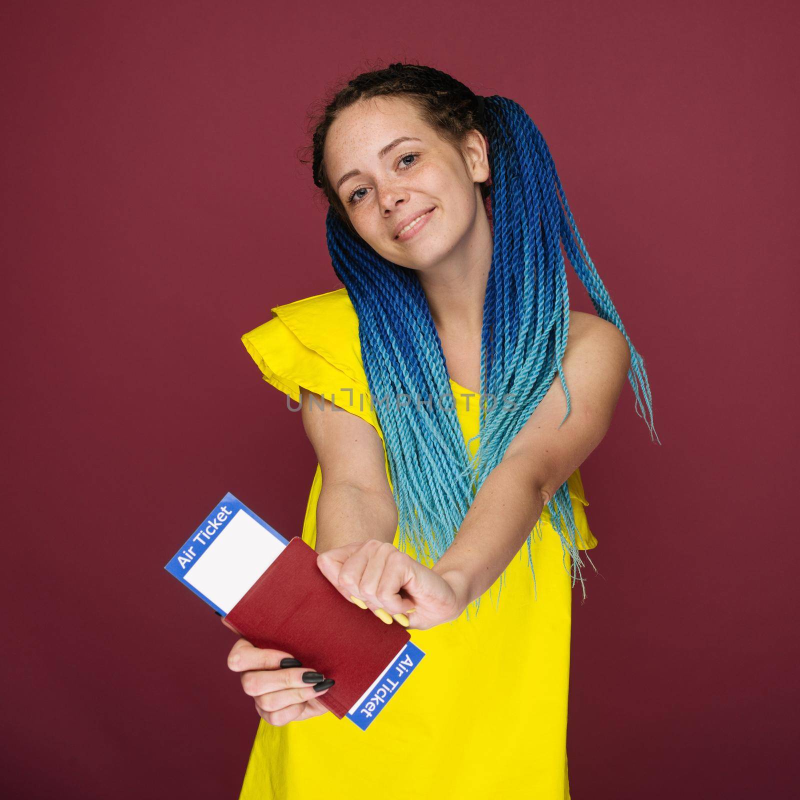 A modern trendy smiling woman in yellow dress with air tickets and a passport in her hand. Young dreamy girl looks at camera. Travel concept