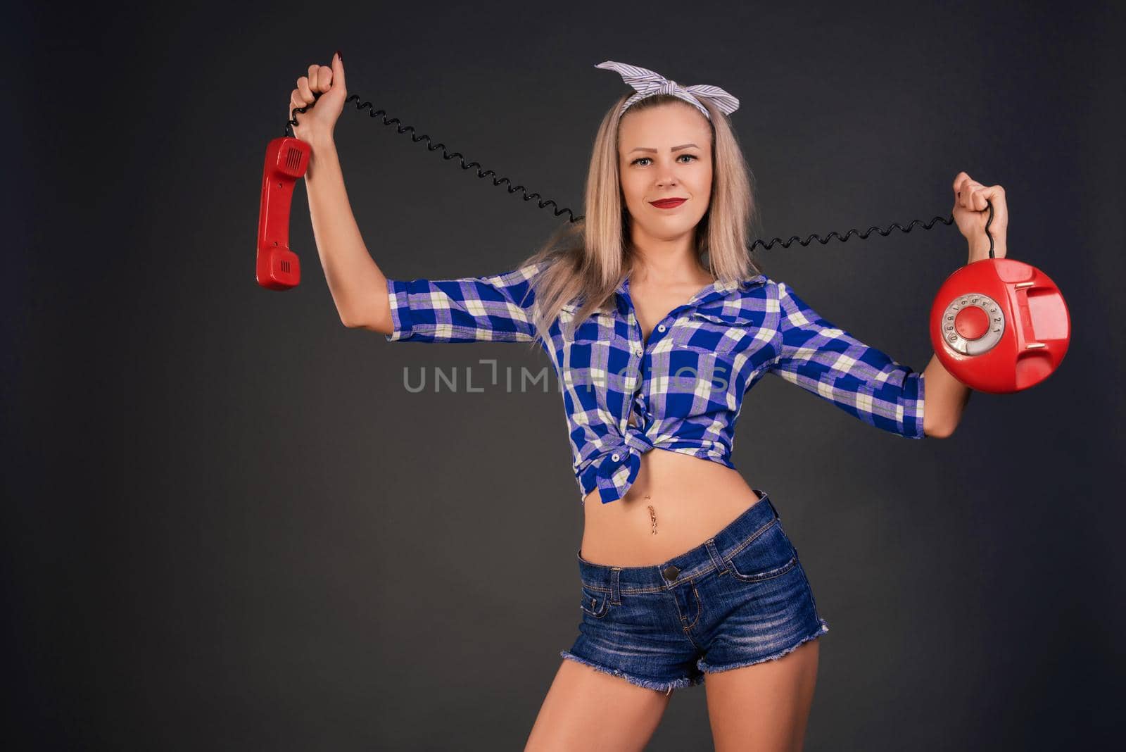 Beautiful slender smile girl in a checkered blue shirt and jeans is holding an old disk phoneisolated on a background