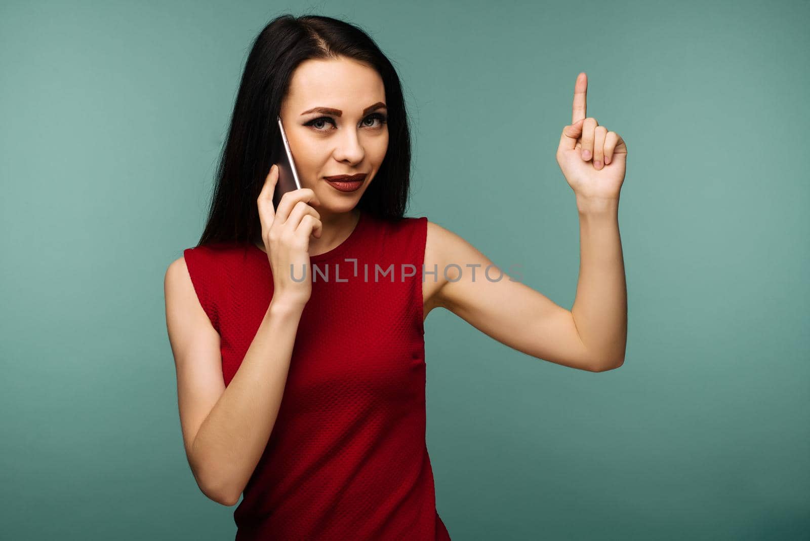 beautiful caucasian surprised young girl talking on her cell phone pointing up isolated background - Image