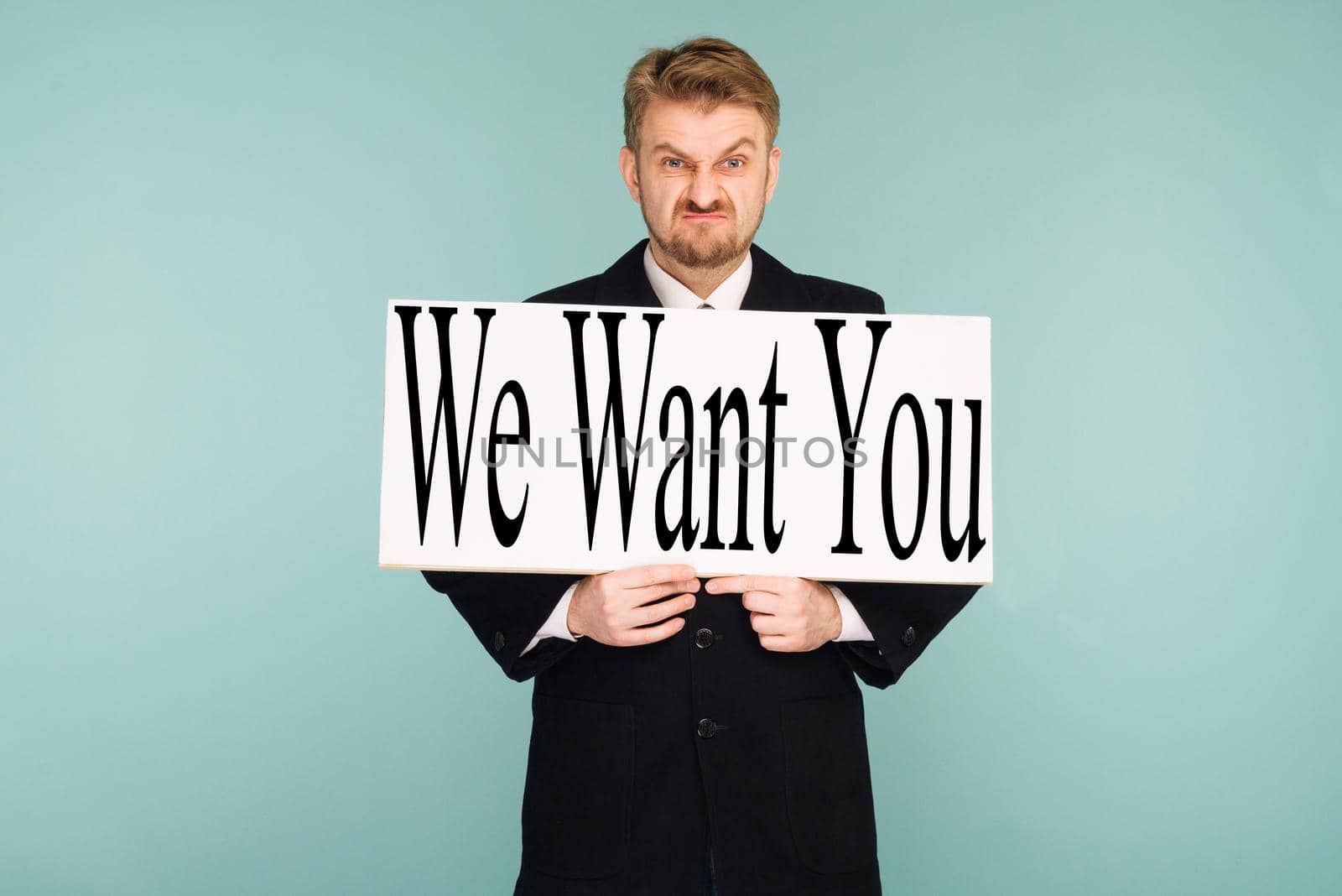 Angry beard young business man showing signboard with sign We Want You, on blue background