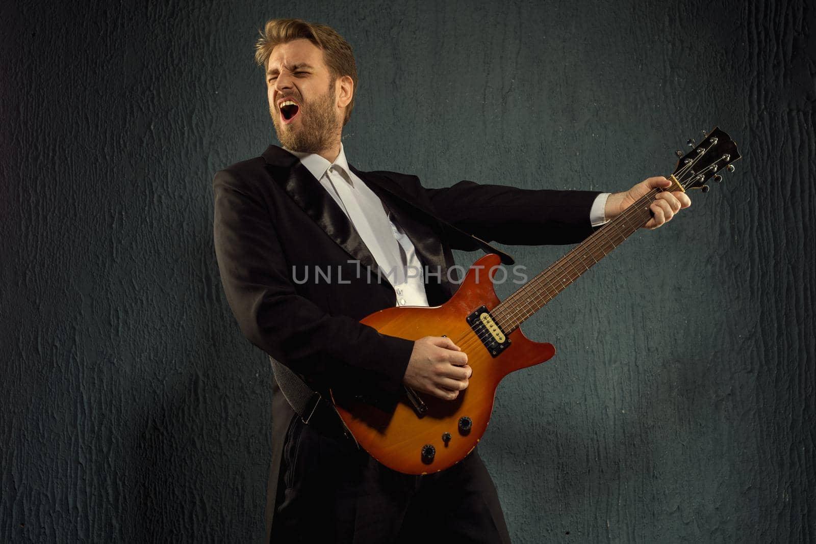 Guitar player with beard and black tailcoat emotionally plays music