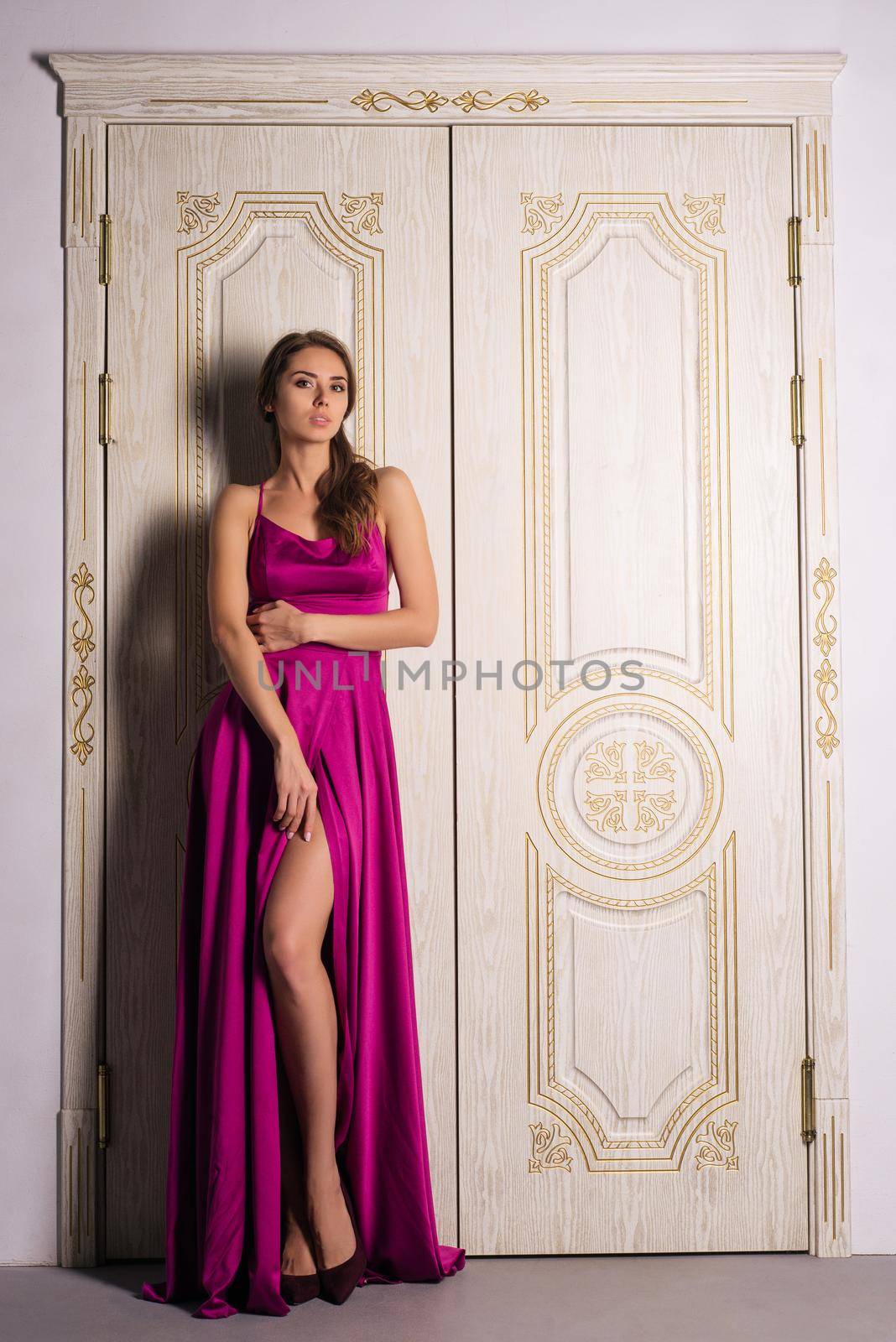 Beautiful girl in long classic red dress posing near old luxury doors. - image