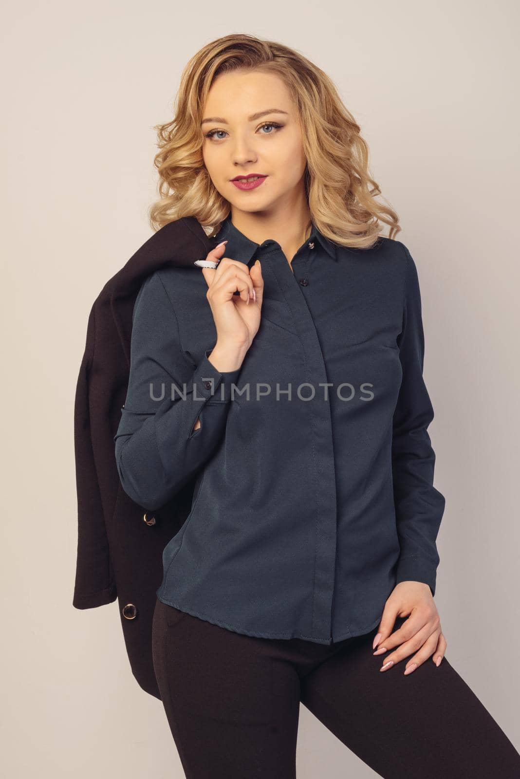 Portrait of a beautiful young business woman standing with hand holding jacket behind her shoulder against grey background. Looking at camera.