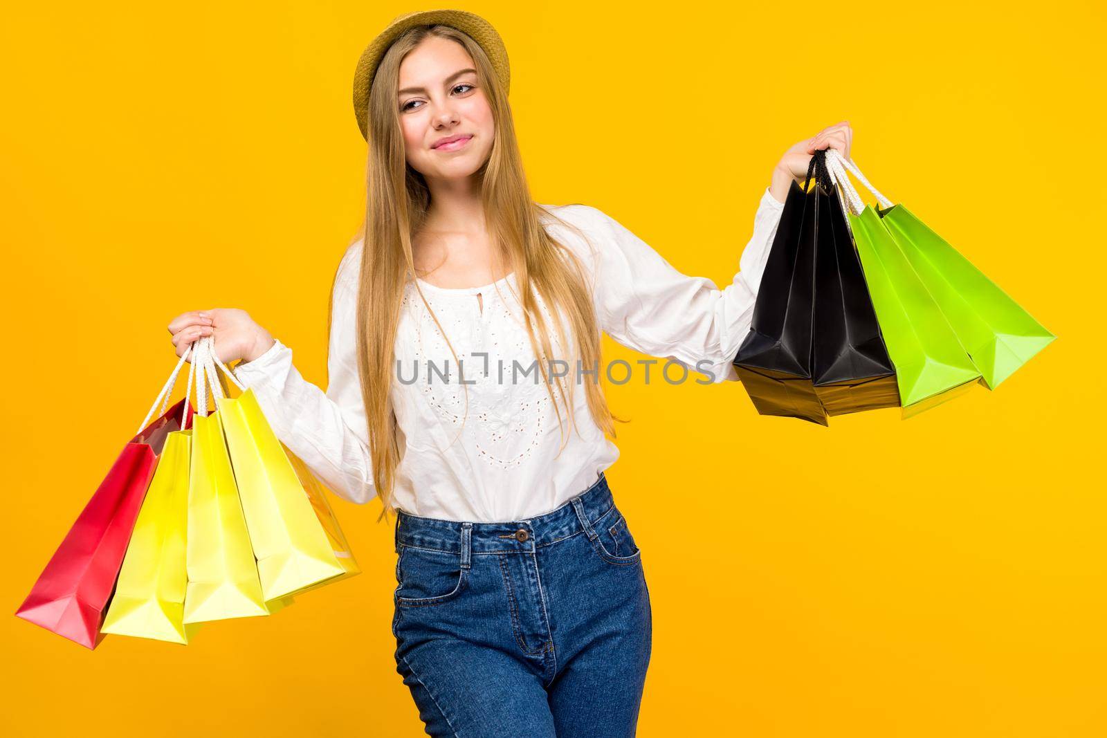 Caucasian teenage girl on yellow background. Stylish young woman with shopping bags in hands - image