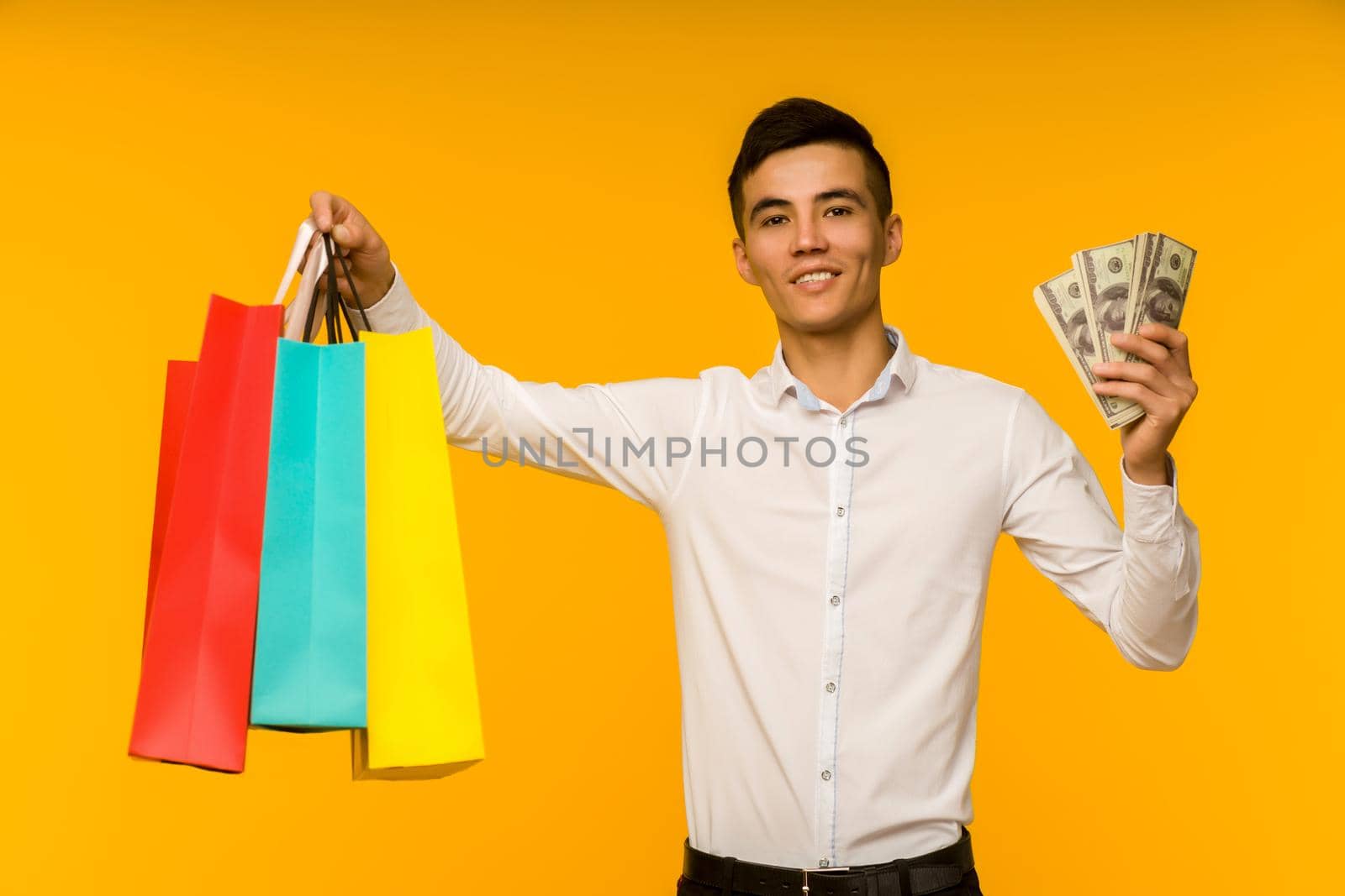 Young asian man showing his shopping bag and money on yellow background