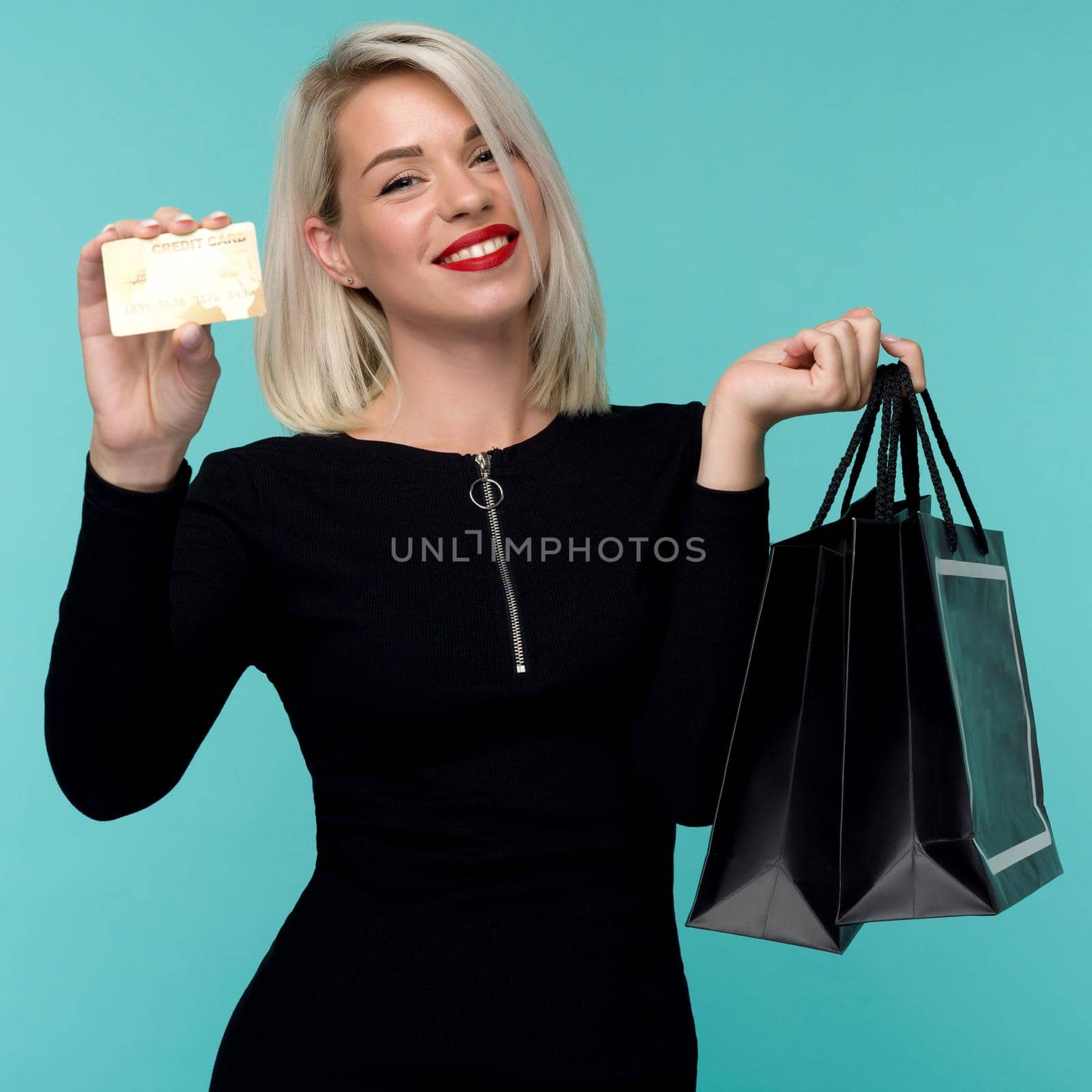 Image of a beautiful happy young blonde woman posing isolated over blue wall background holding shopping bags. Black Friday Holiday Concept. Sale