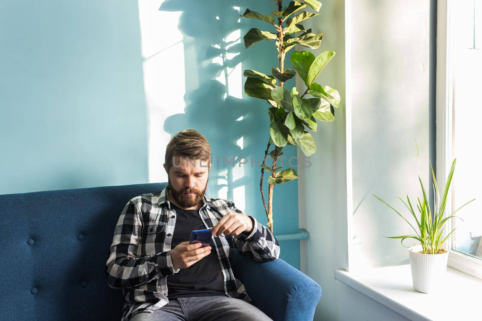 Technologies and leisure concept - Handsome man using smartphone sitting at home