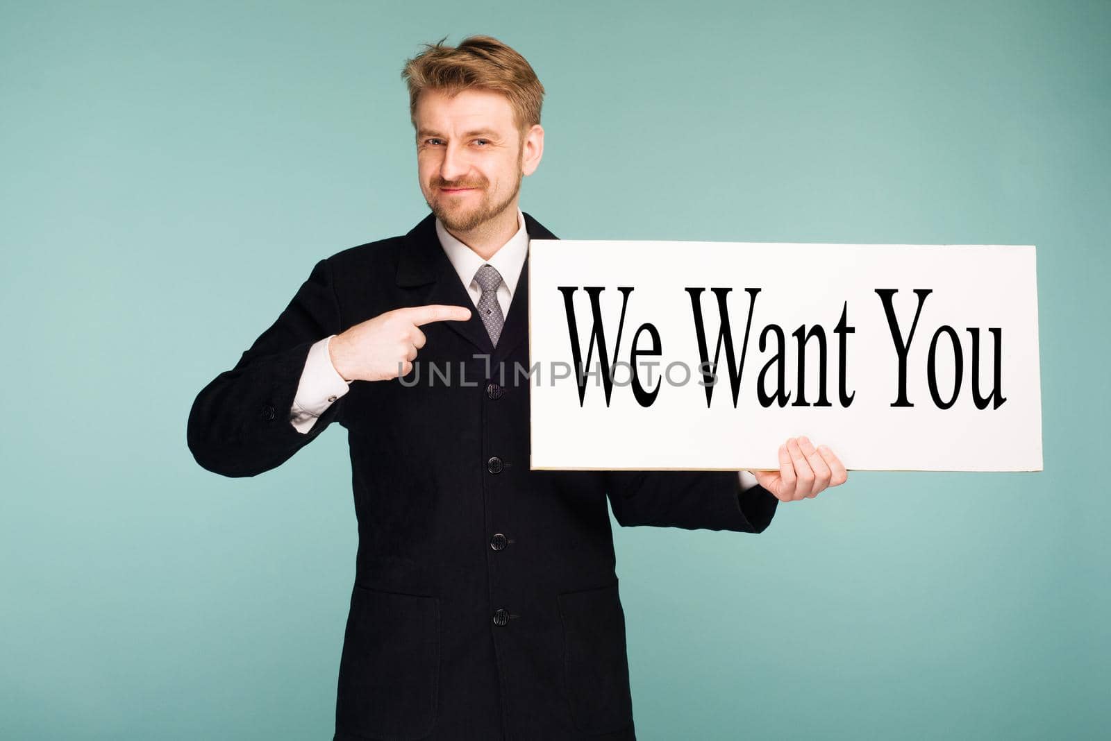 Happy smiling young business man points finger signboard with sign We Want You, on blue background