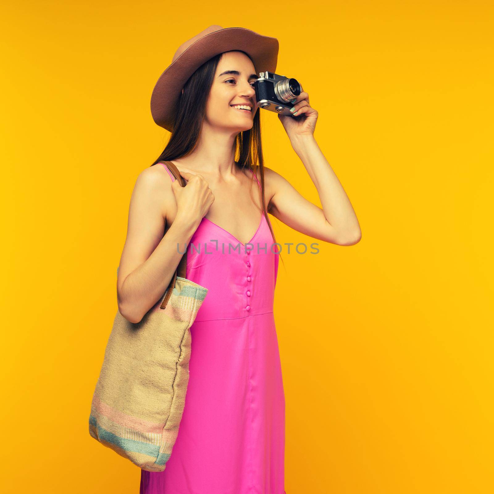 Happy girl in a pink dress and sunglasses holding camera on a yellow background by zartarn