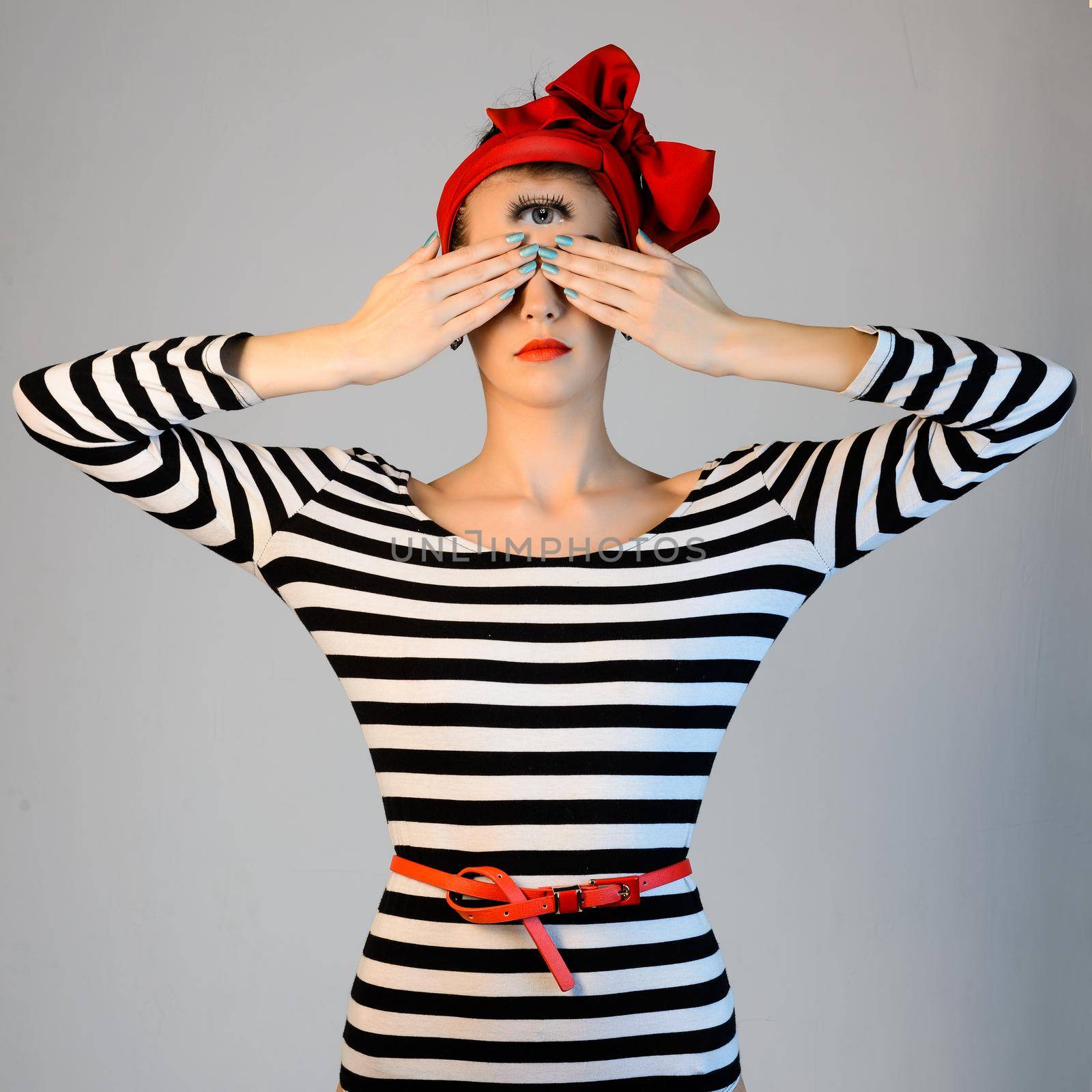 Beautiful girl in a striped dress and a red turban on her head is covering his eyes with hands and looks esoteric third eye on her forehead.