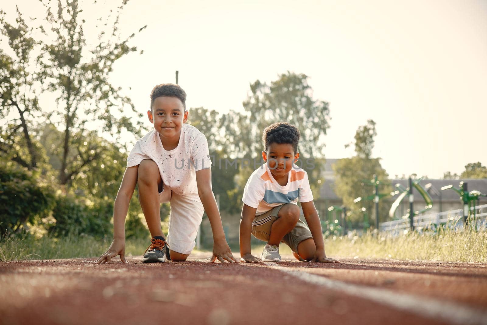 Two multiracional brothers are going to run at the stadium. Boys wearing a white t-shirts. Boys are ready to run hundred meters.