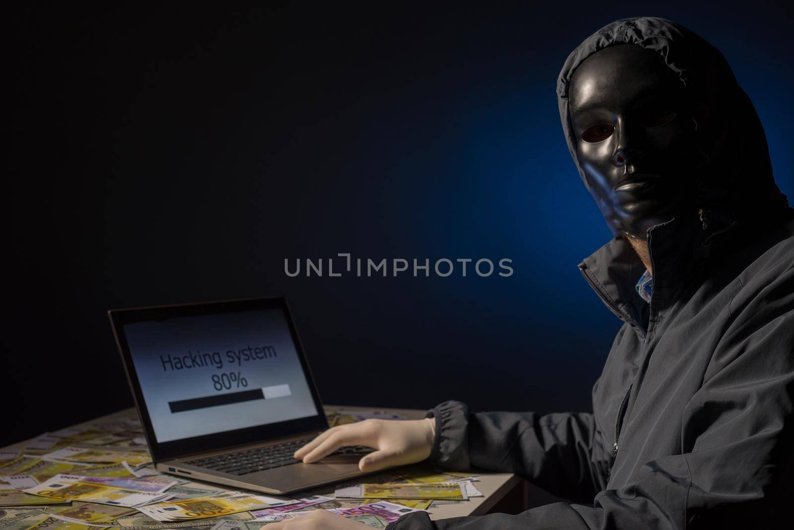 Anonymous hacker programmer uses a laptop to hack the system in the dark. The concept of cybercrime and hacking database. Money is scattered on the table. Focus on laptop