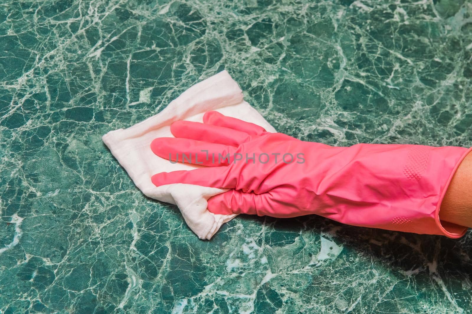 Housewife's hand in a pink household glove wipes a green marble surface with a white cloth in the kitchen by AYDO8