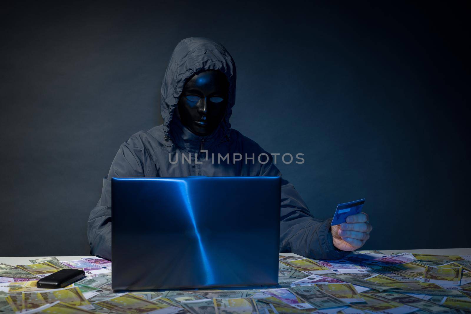 Anonymous hacker in mask programmer uses a laptop to hack the system in the dark. The concept of cybercrime theft of money from bank cards