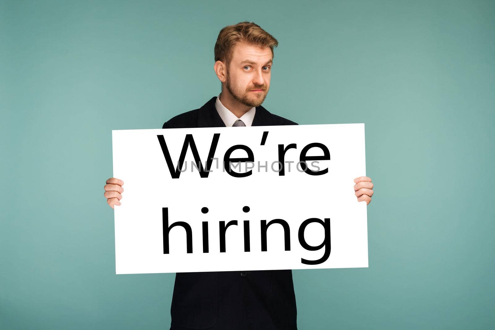 Happy smiling young business man showing signboard with sign we hiring, on blue background