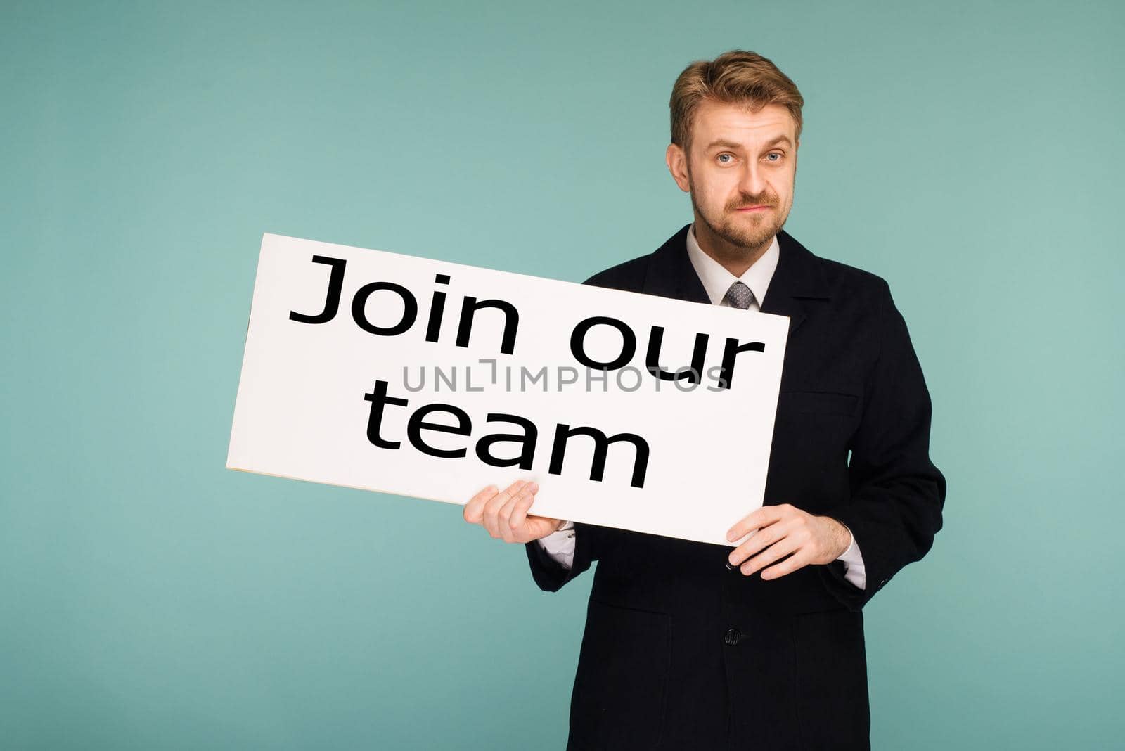 Happy smiling young business man showing signboard with sign Join Our Team, on blue background